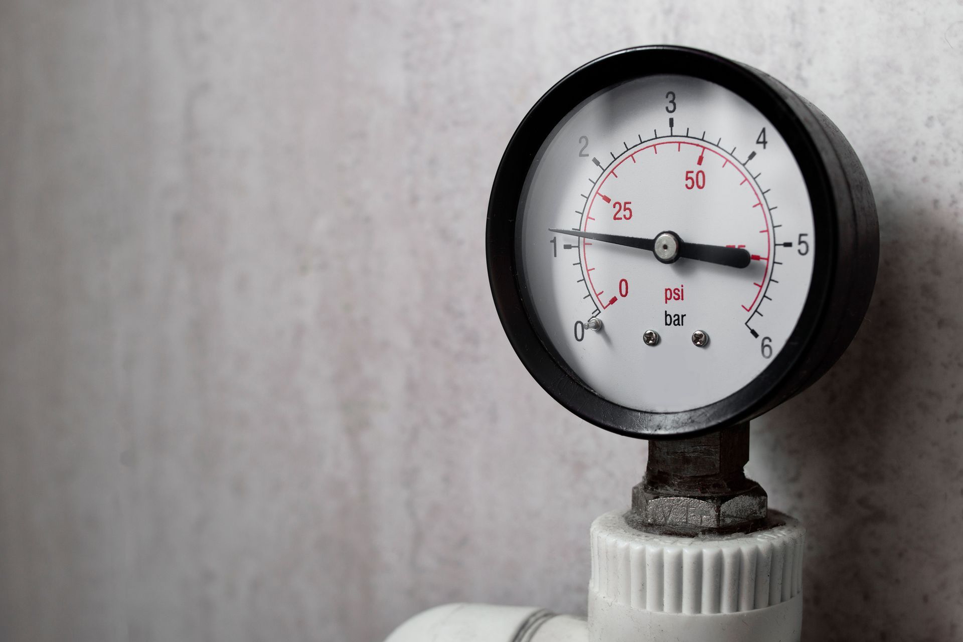 Close-up of a pressure gauge with a black rim and white dial mounted on a pipe