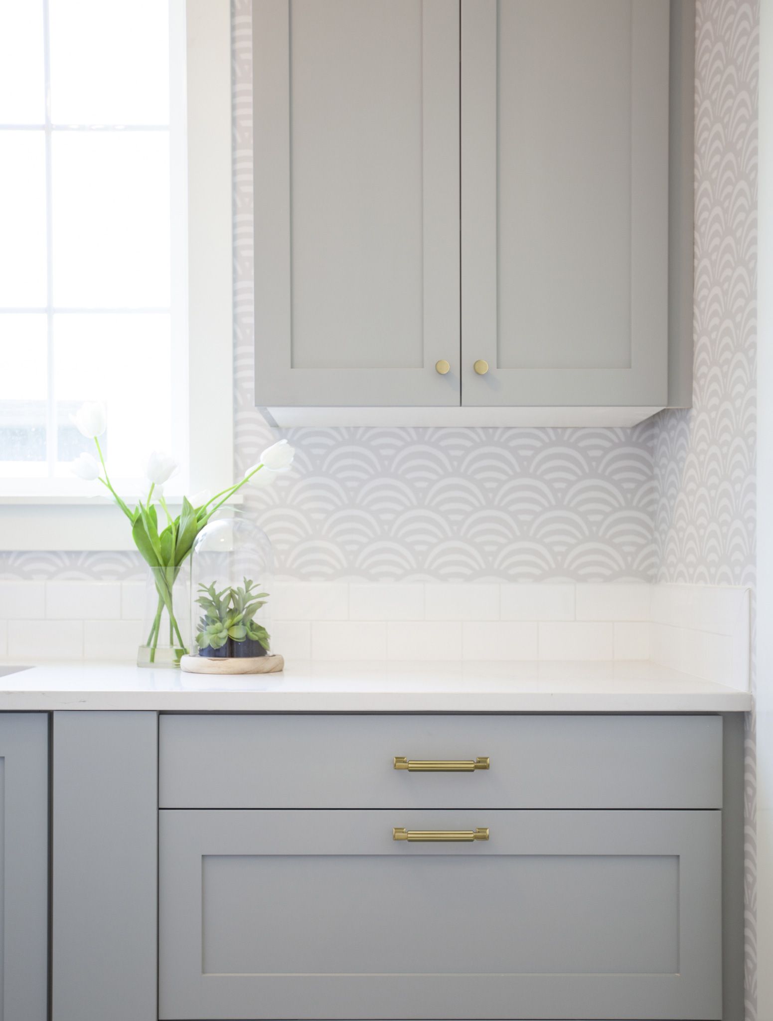 A laundry room with gray cabinets , white counter tops , and a window.