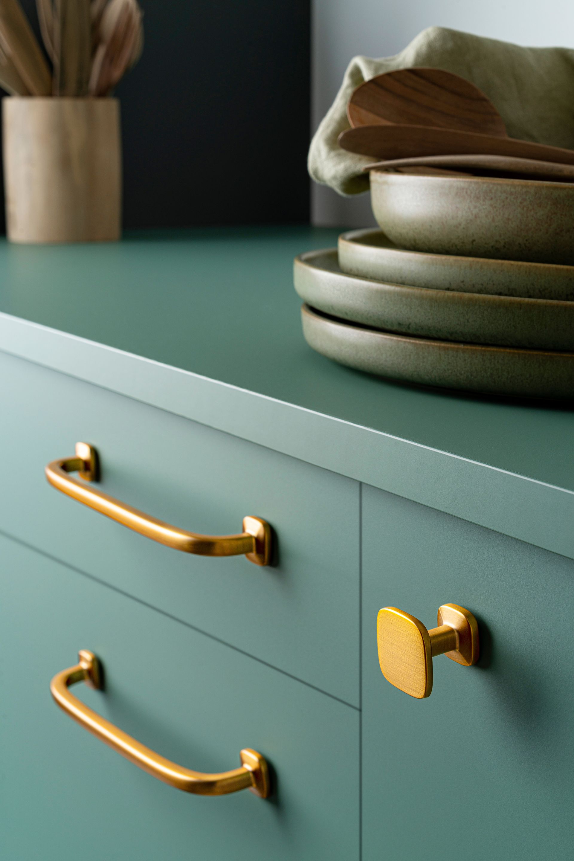 A kitchen counter with green cabinets and gold handles.
