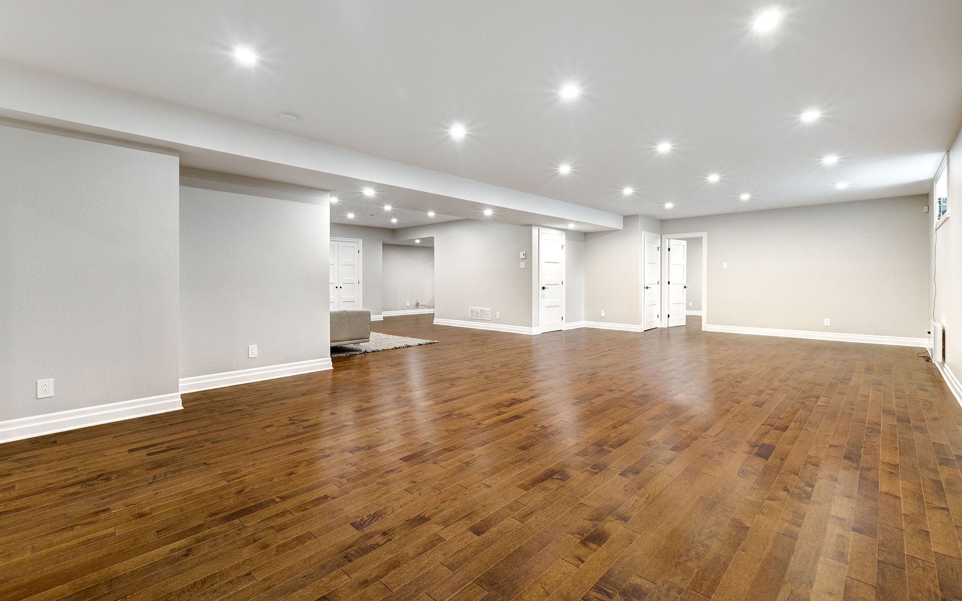 An empty basement with hardwood floors and white walls.