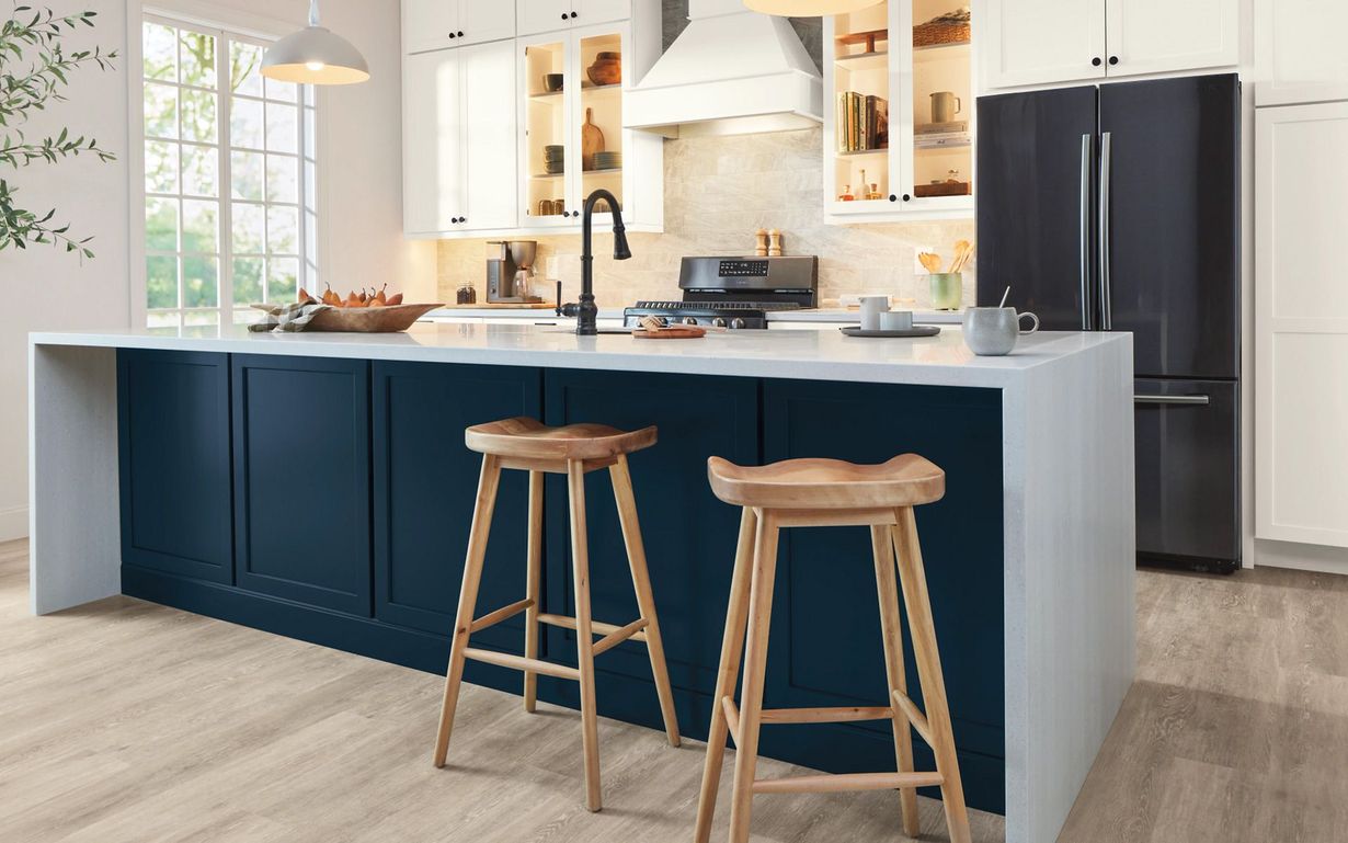A kitchen with blue cabinets , wooden stools , a refrigerator , and a stove.
