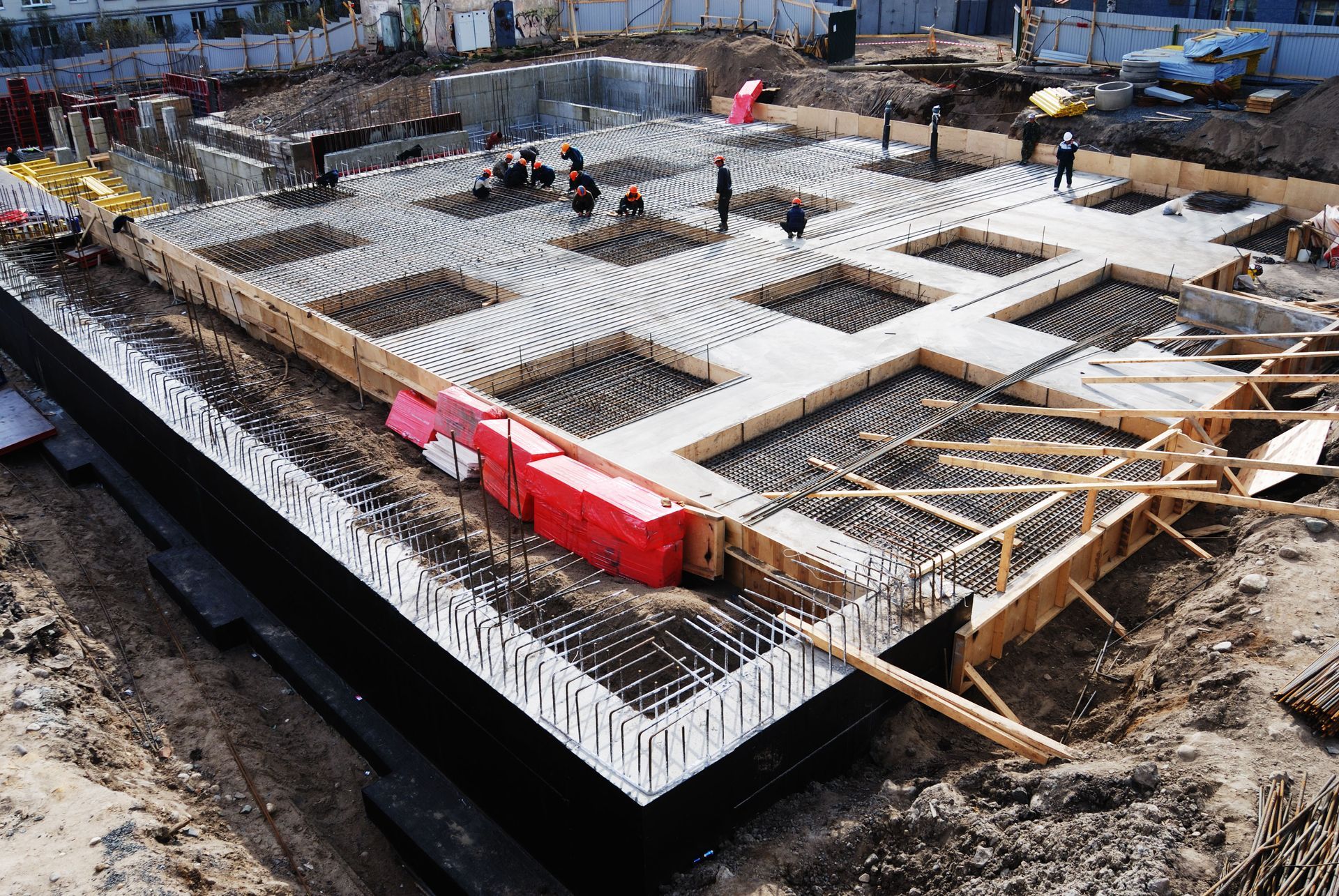 Construction site with workers, concrete foundation with rebar, wooden forms, and materials.
