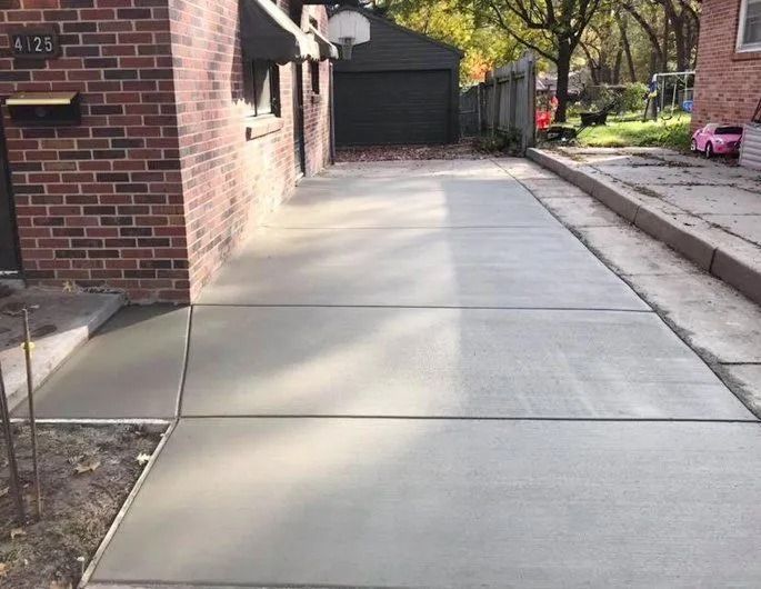Freshly poured concrete driveway and sidewalk next to a brick house.