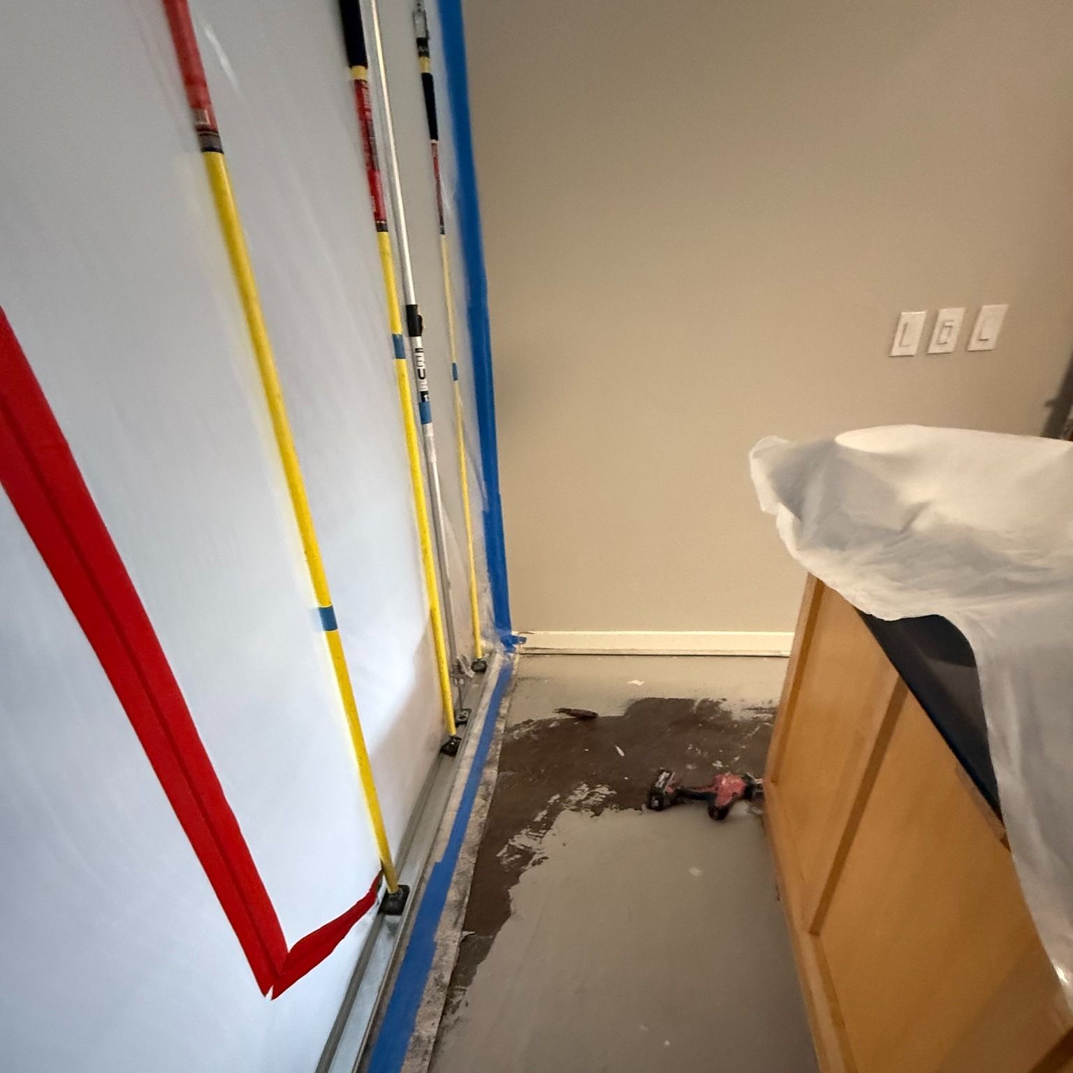 Room interior with taped walls, paint rollers, and a cabinet covered in plastic.