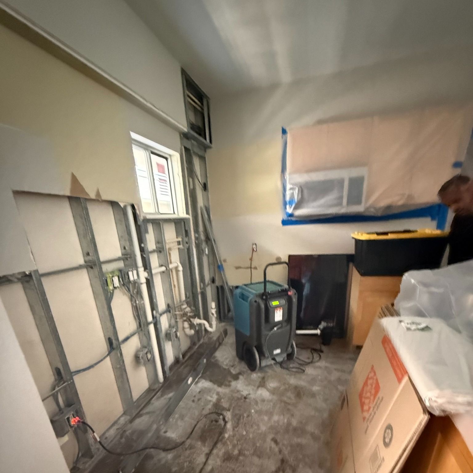Room under renovation; exposed metal studs, drywall, dehumidifier, window taped off, various boxes and materials.