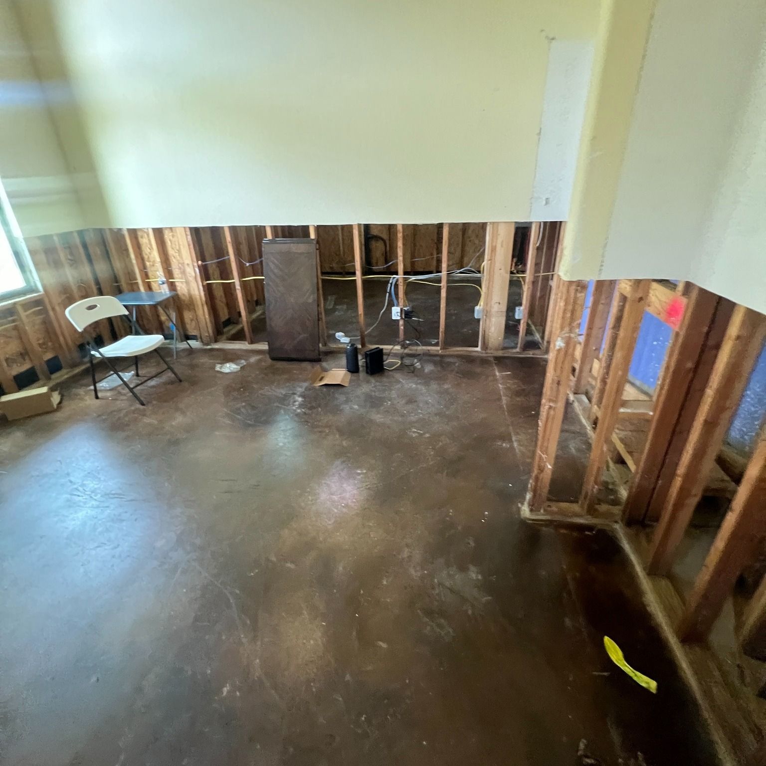 Room with exposed studs, damp floor, damaged walls, and a chair.
