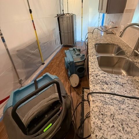 Water damage restoration in a kitchen: equipment, plastic sheeting, and a stainless steel sink.