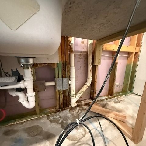 Under-sink area, open wall, exposed plumbing and electrical. White sink, gray pipes, studs, and insulation visible.