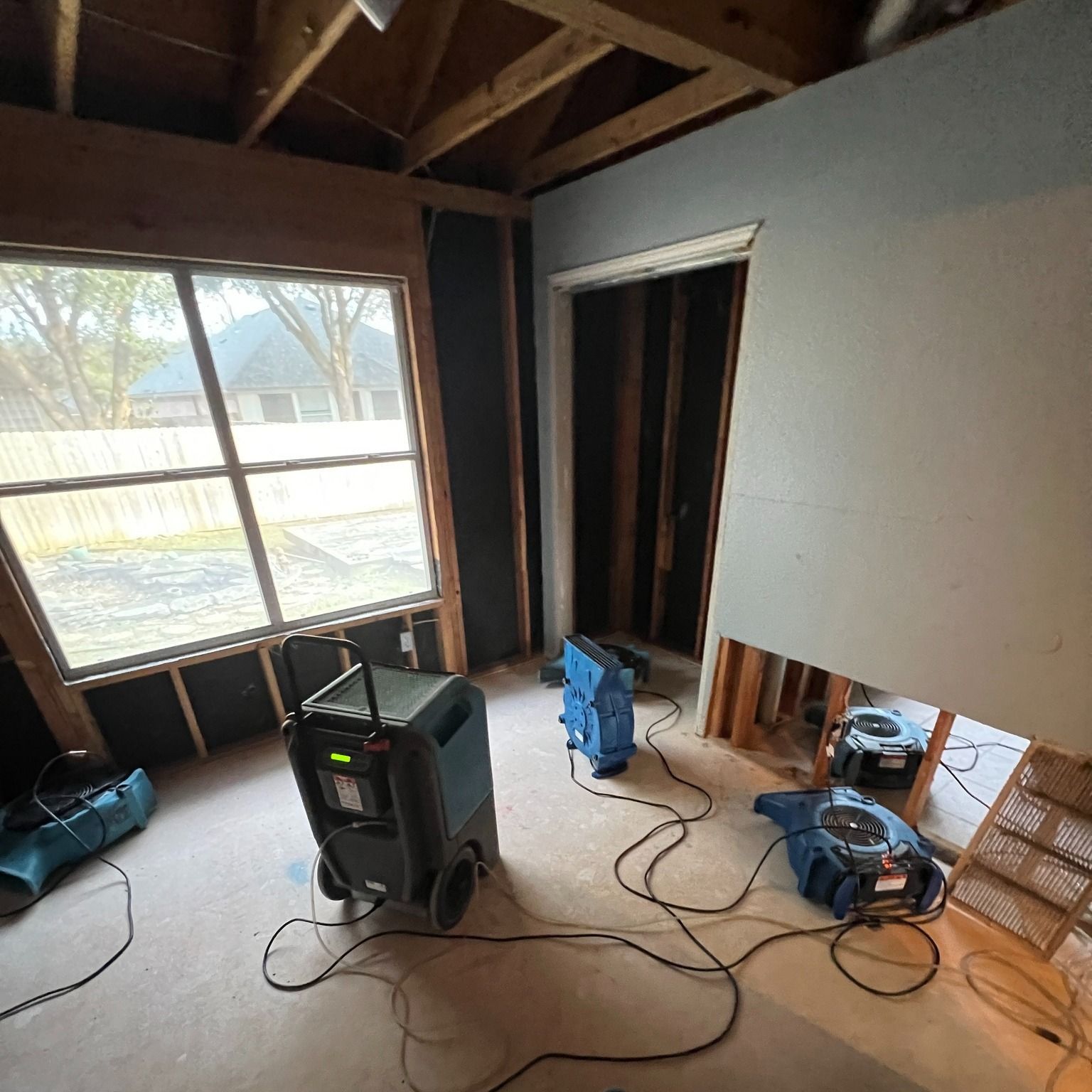 Room undergoing restoration with dehumidifiers running, walls and ceiling exposed.