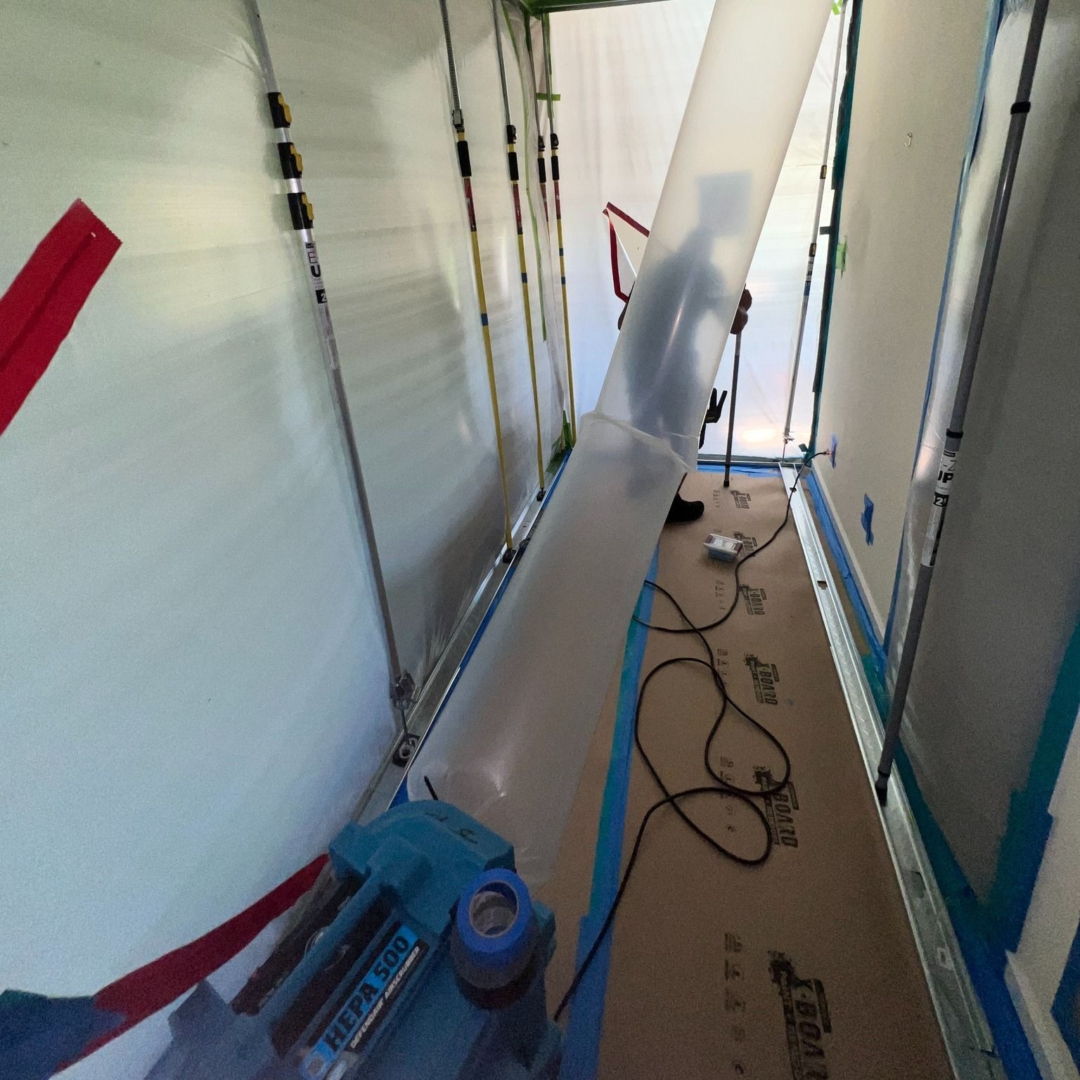 Blue dehumidifier and ventilation duct inside a plastic-covered construction corridor.