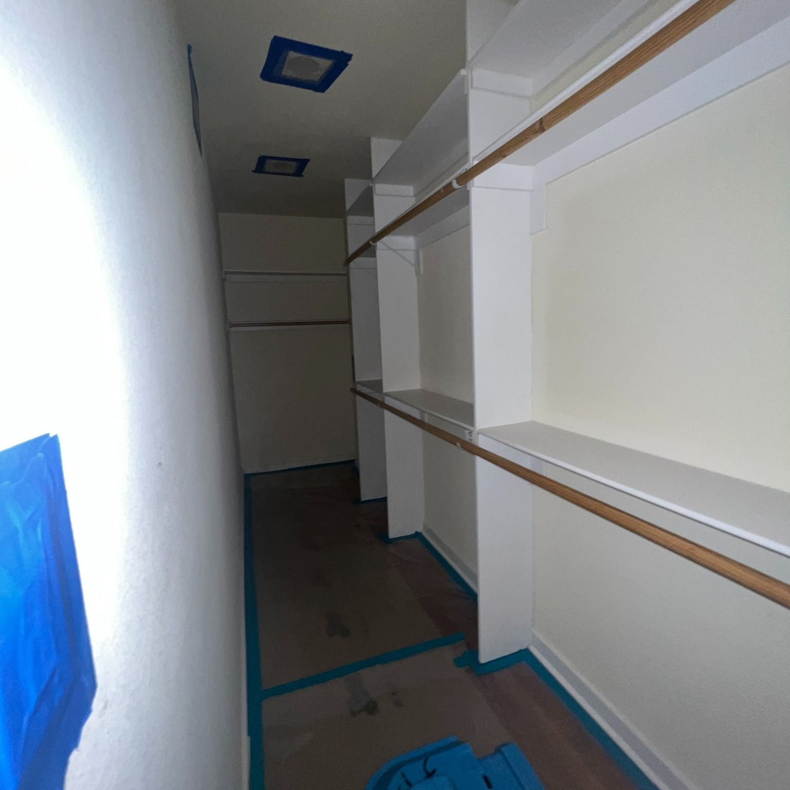 Empty walk-in closet with shelves and rods, white walls, and blue painter's tape on the floor.