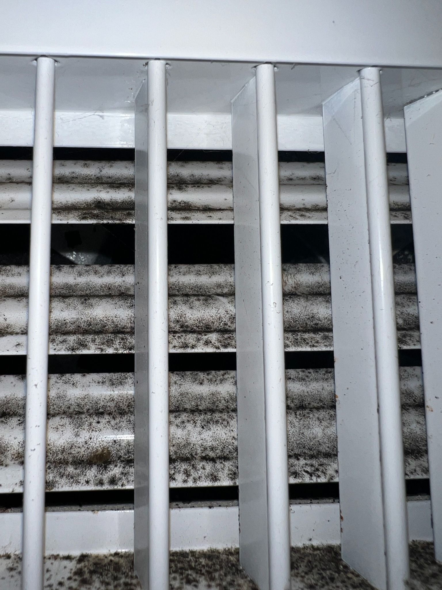 Close-up of a white air vent with visible black dust and debris.