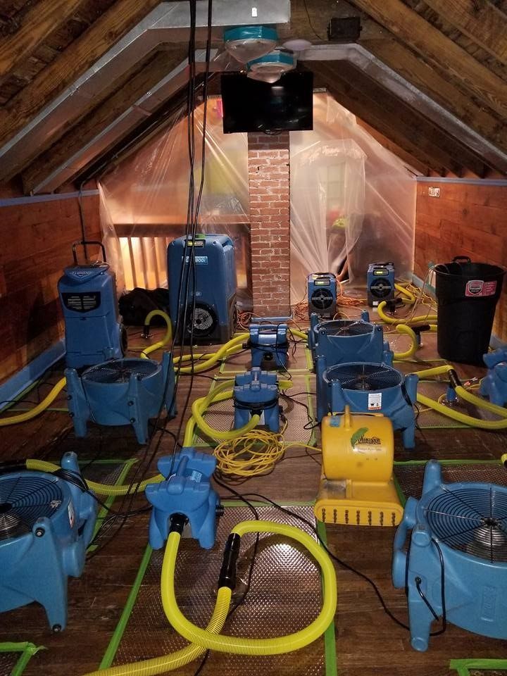 Attic with multiple blue and yellow dehumidifiers and fans, set up for water damage restoration.