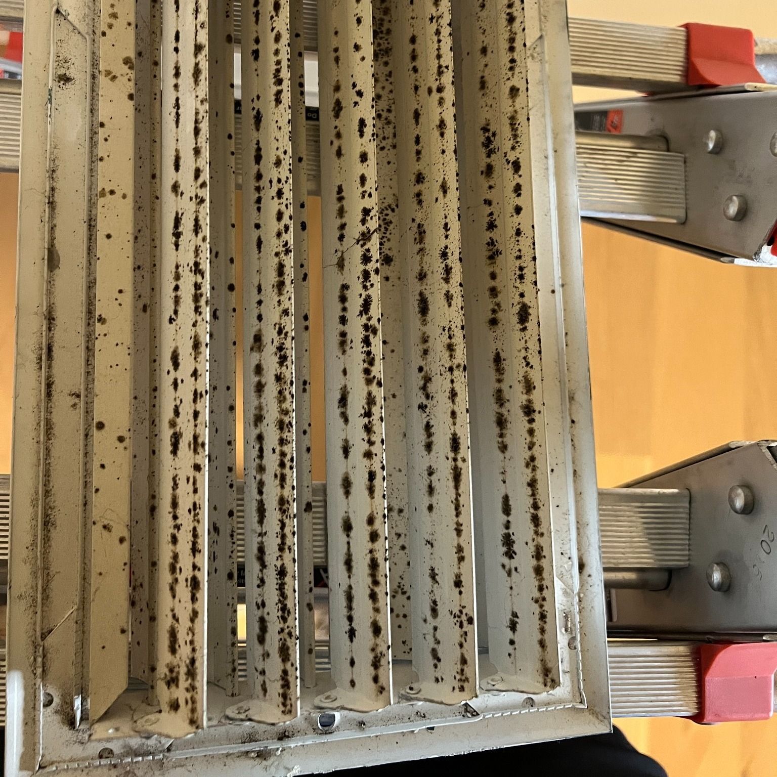 Close-up of a dirty air vent. Metal slats have dark spots of grime.