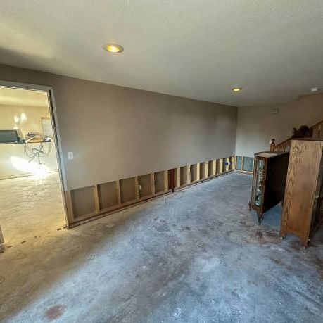 Room undergoing renovation. Exposed studs along a wall. Concrete floor. An open doorway and cabinet are also visible.