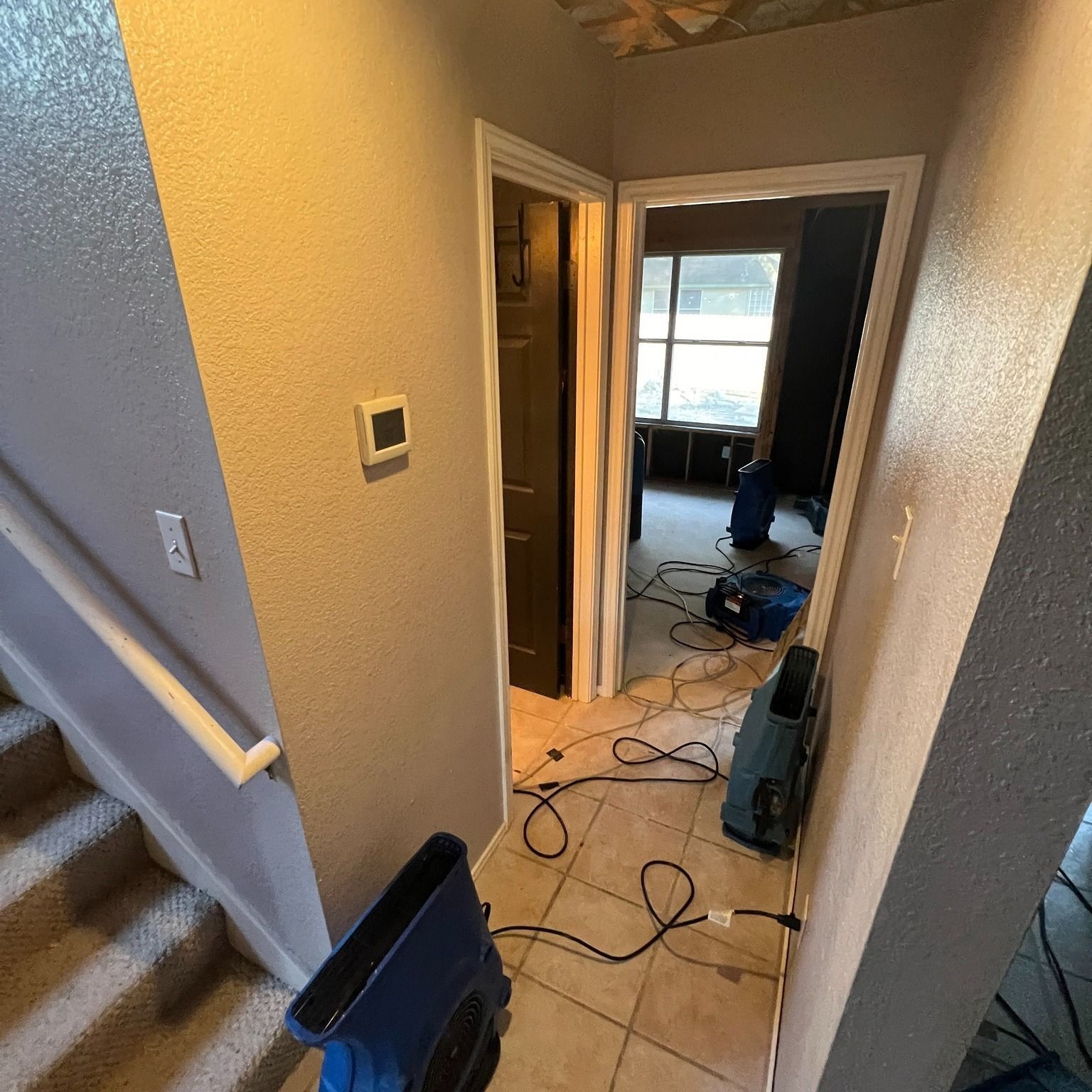 Hallway with door open to a room with drying equipment. Stairs to the left, and walls are beige.