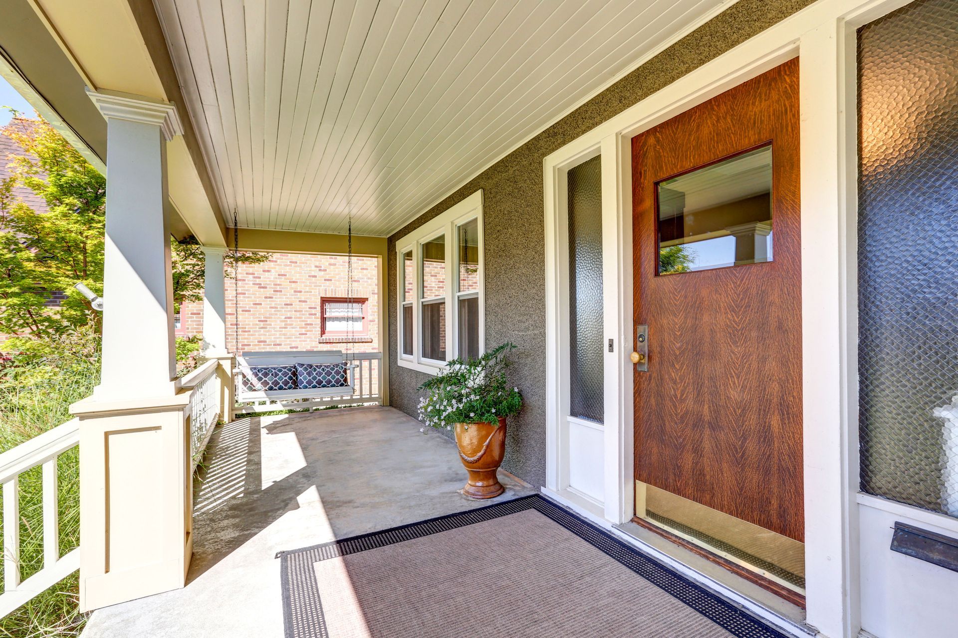The front porch of a house with a wooden door and a white railing.