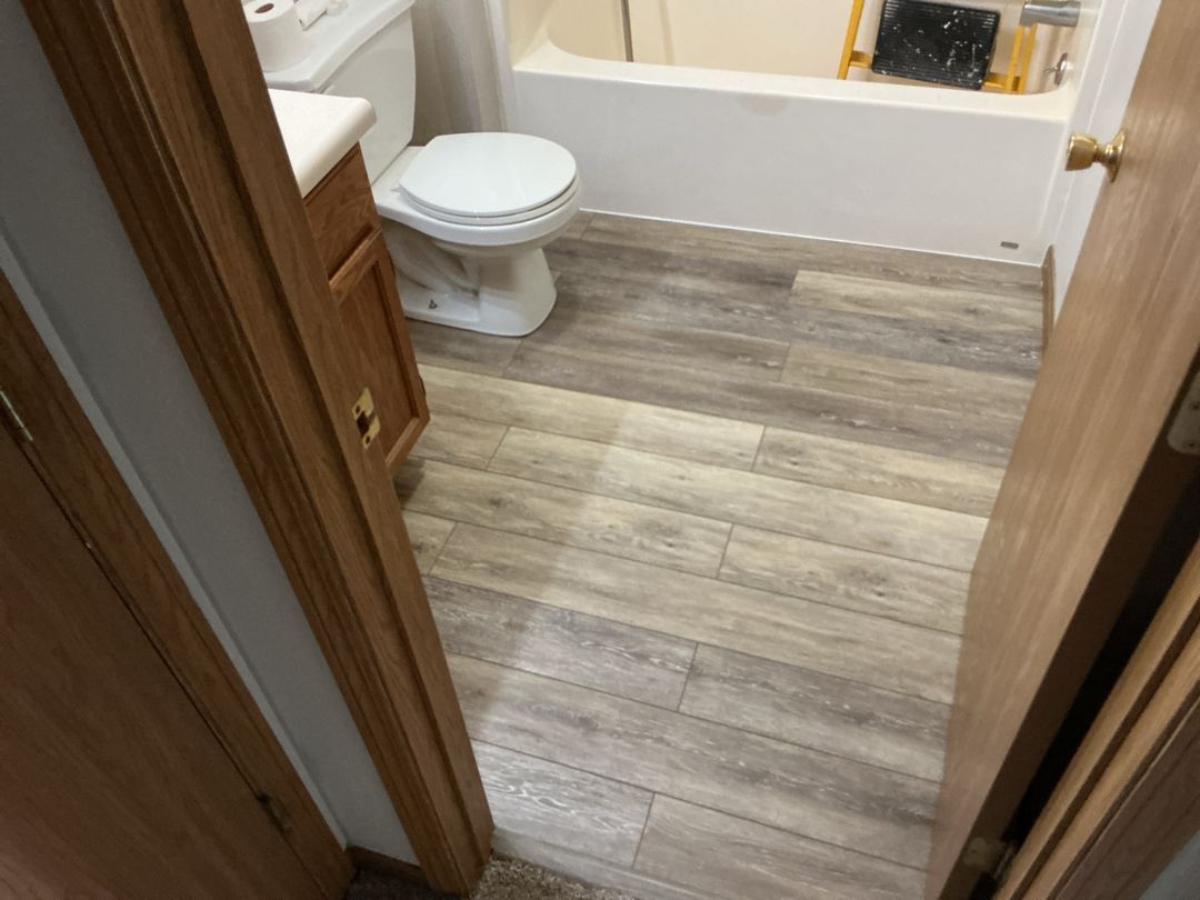 Bathroom with wood-look flooring. Toilet, vanity, and bathtub visible. Door frame in view.