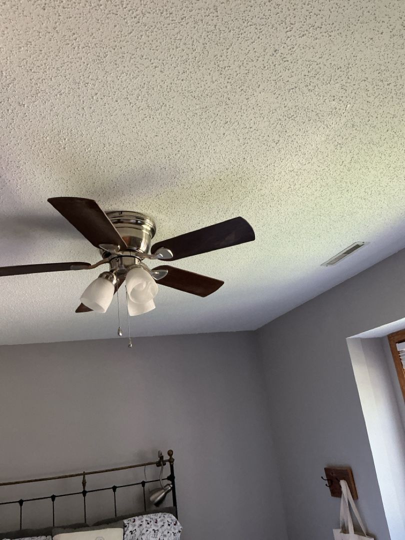 Ceiling fan with dark blades and lights in a room with gray walls and a textured ceiling.