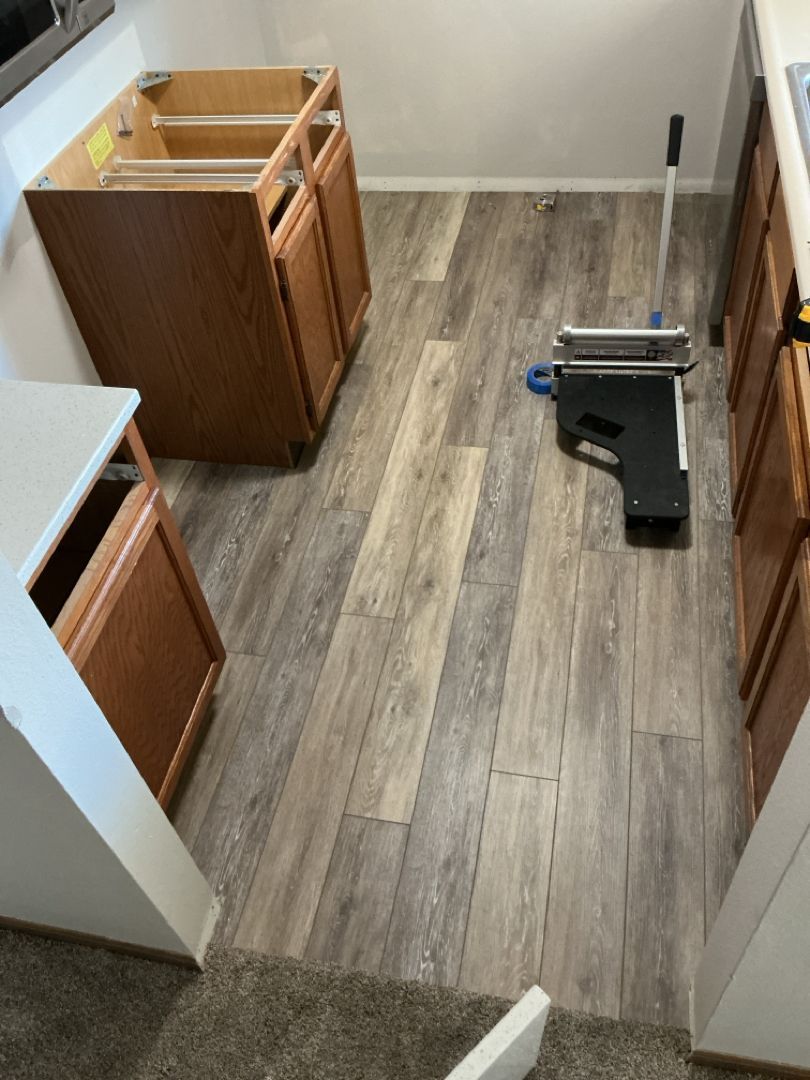 Kitchen with new wood-look flooring installed. Cabinets are present, along with a flooring installation tool.