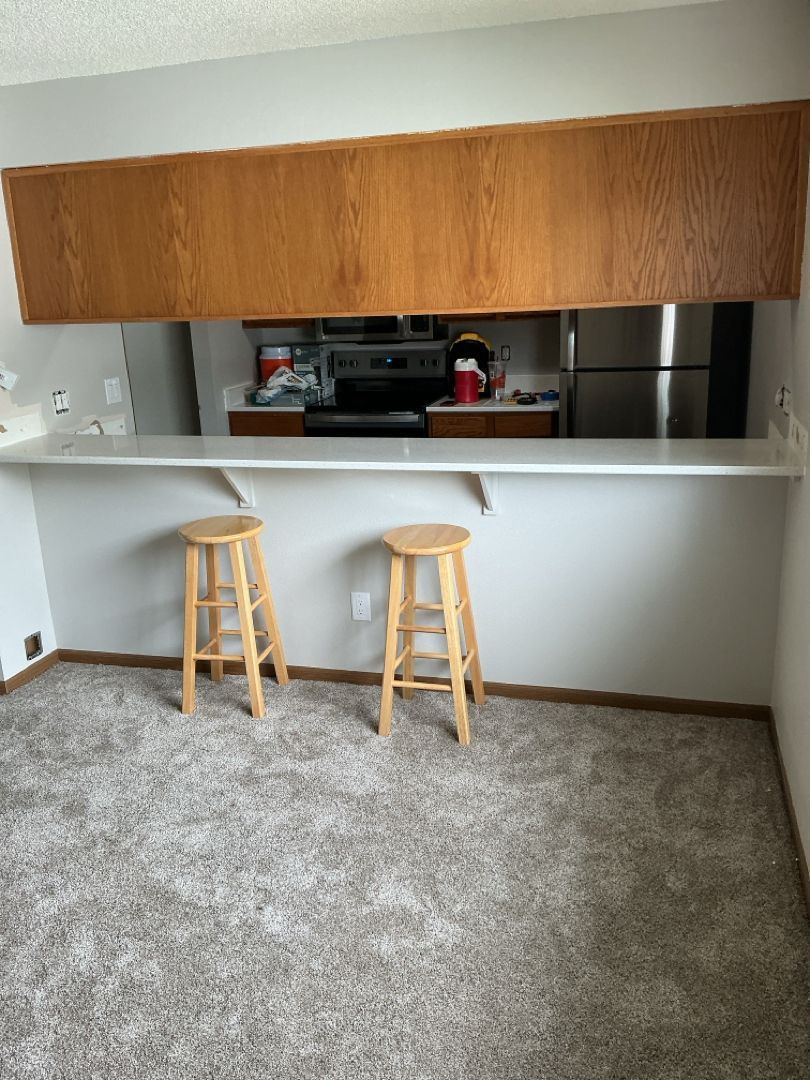 Two wooden stools at a kitchen bar. Overhead wooden cabinetry with an opening to the kitchen.