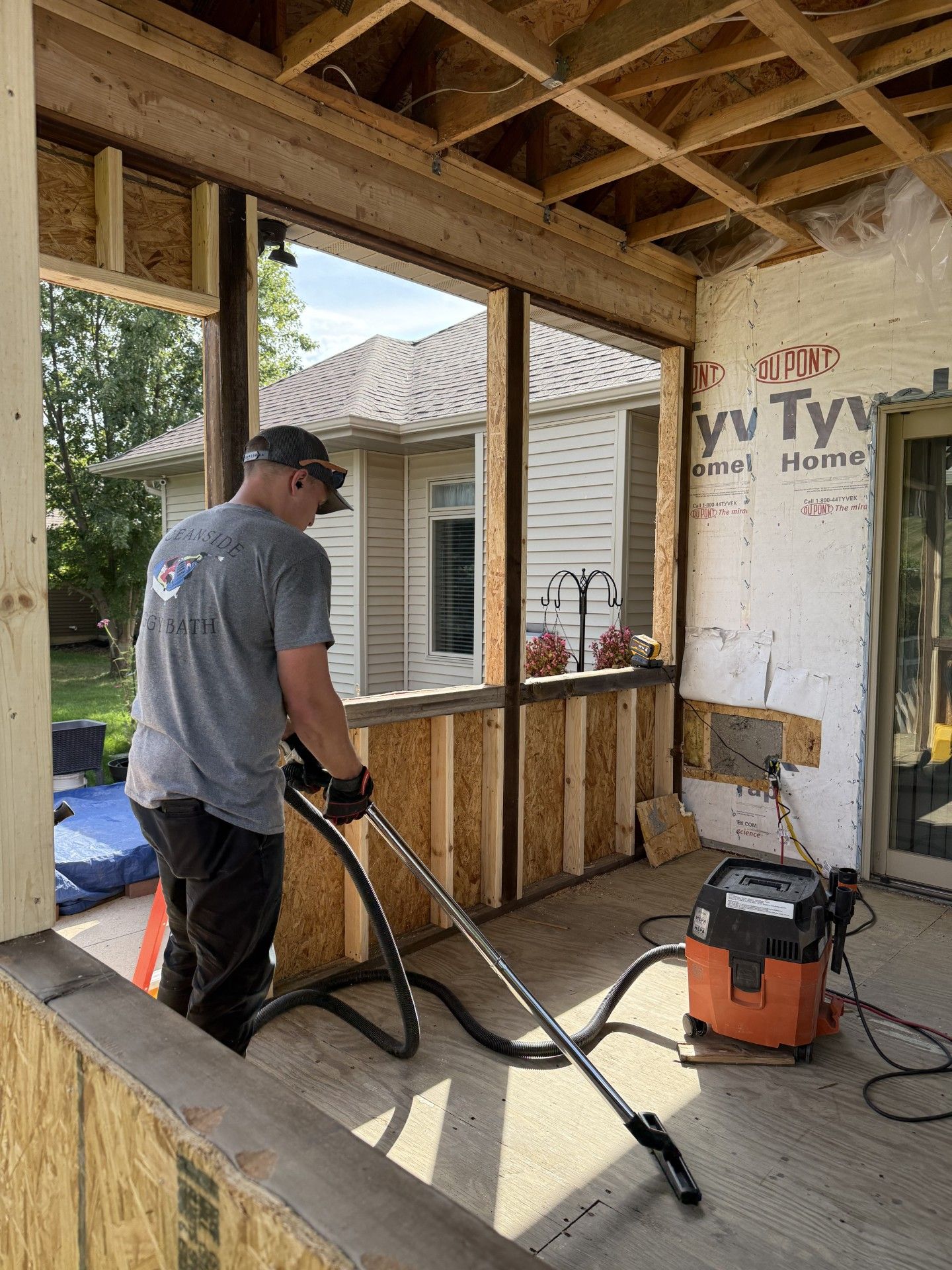 Person vacuums an unfinished porch. Building is under construction. Outdoors, daytime.