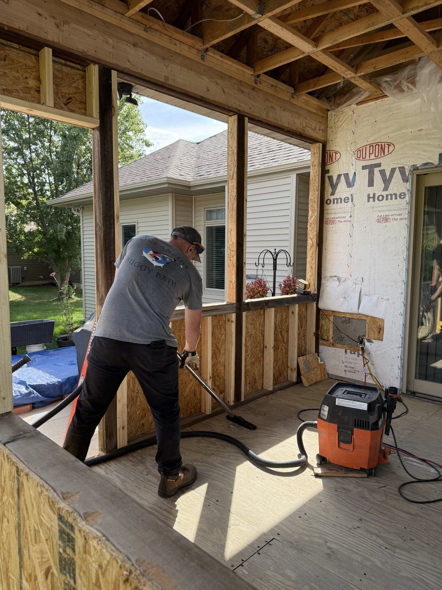 Person vacuuming inside a porch under construction. The porch has exposed wood framing.