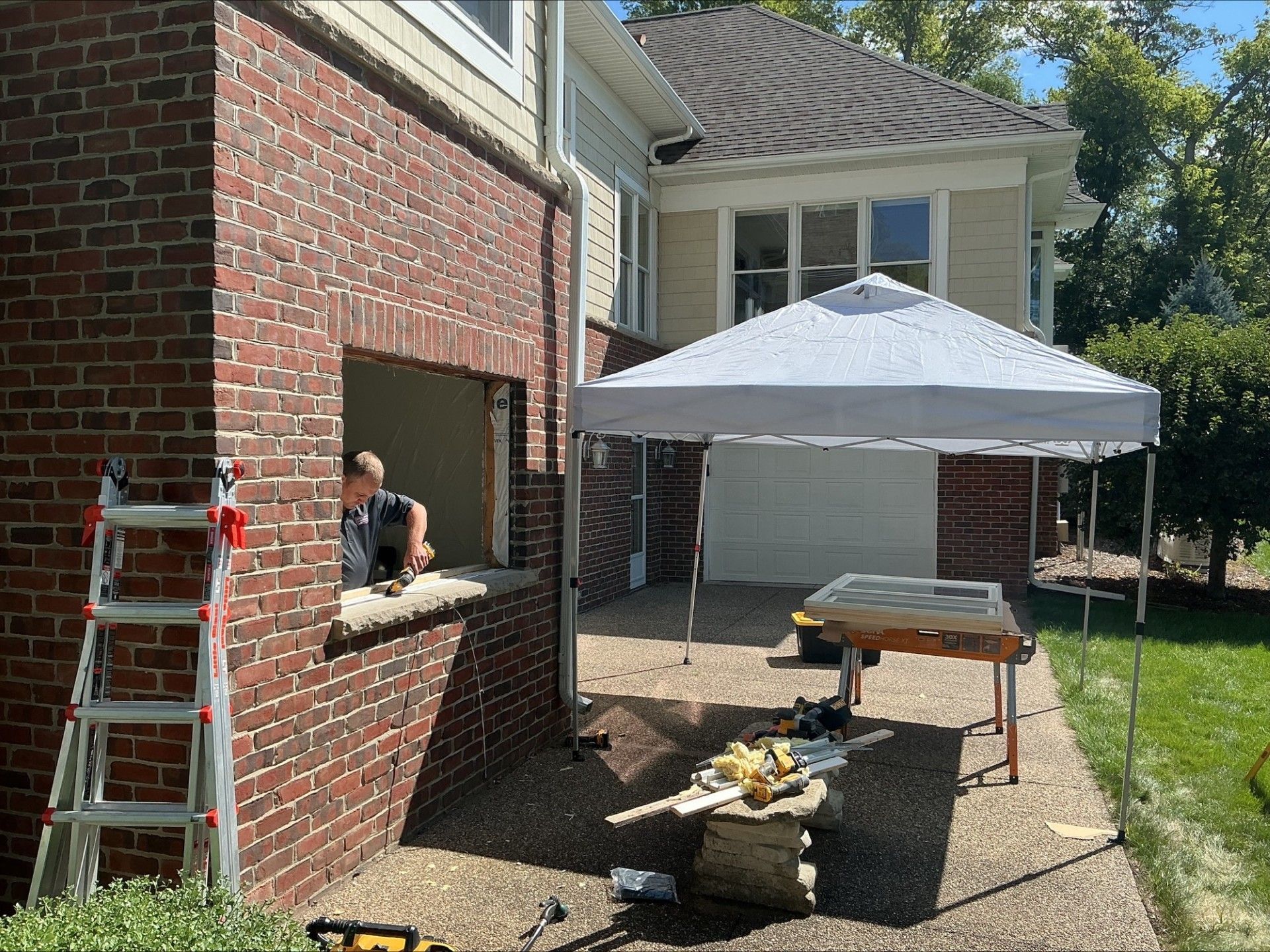Construction site with open brick wall, worker, ladder, and canopy tent in front of a house.