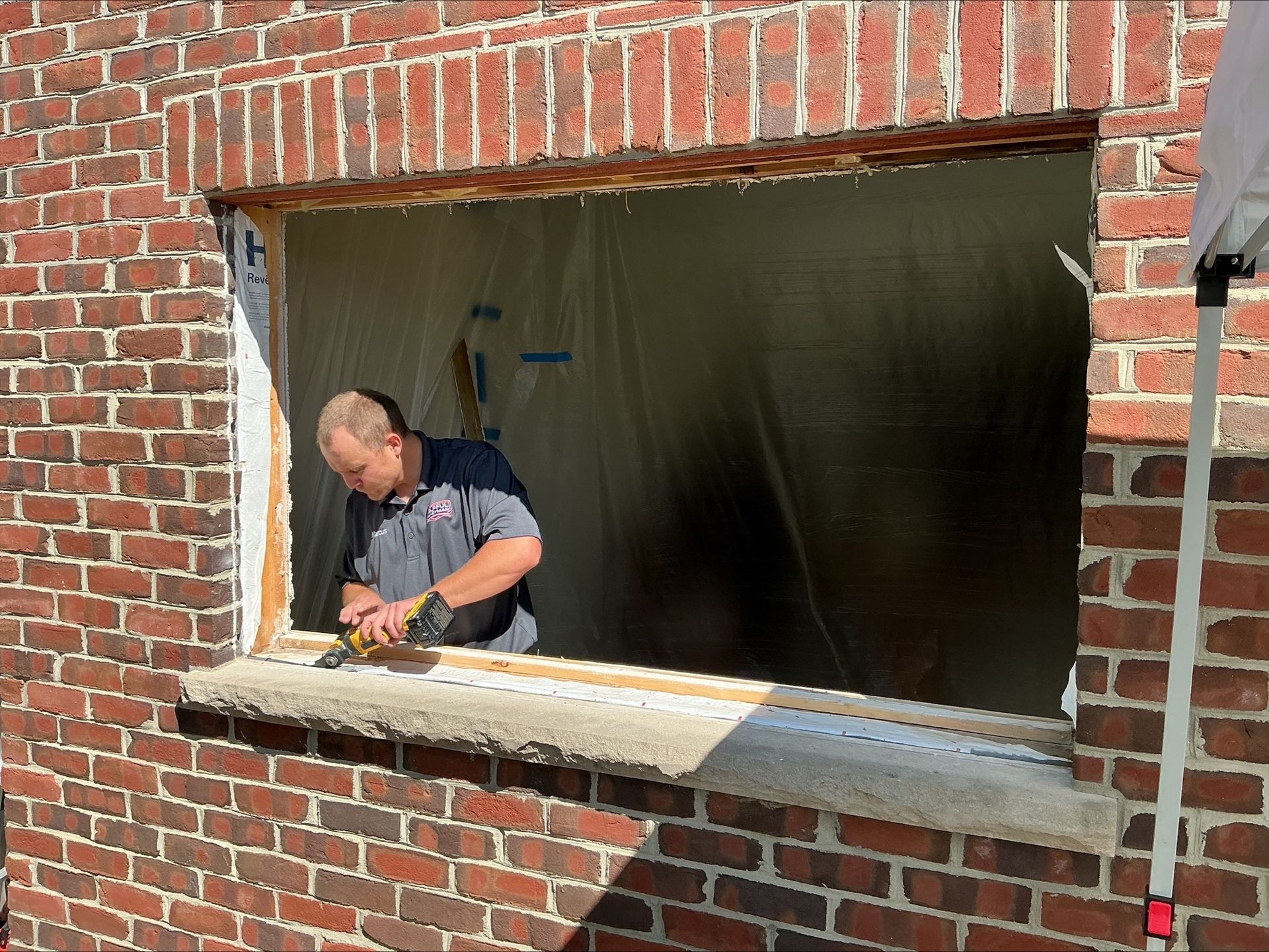Man using tool on window frame within brick building.