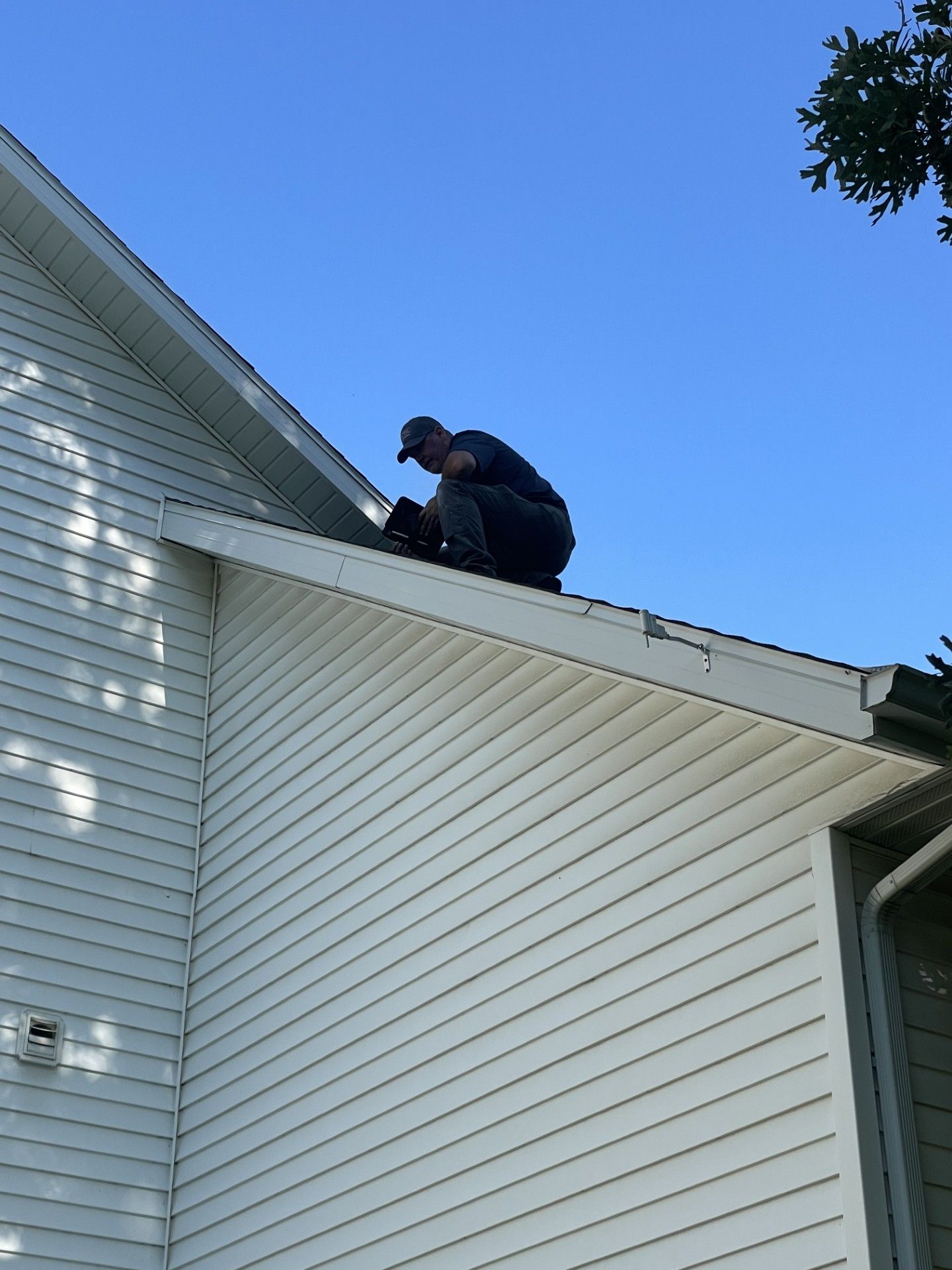 Person on a roof working on the roof trim. White house, blue sky.