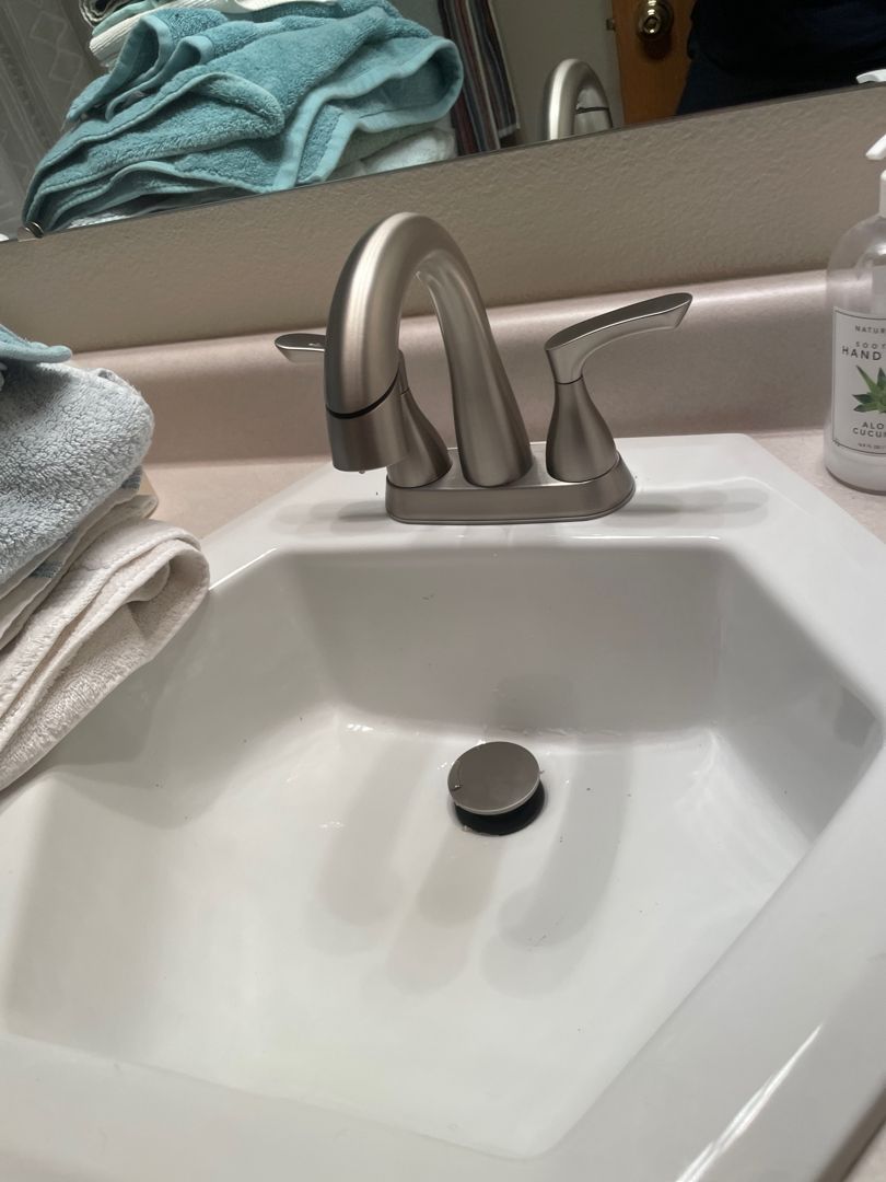Bathroom sink with faucet and soap dispenser. White sink, brushed nickel faucet, light pink countertop, and towels.