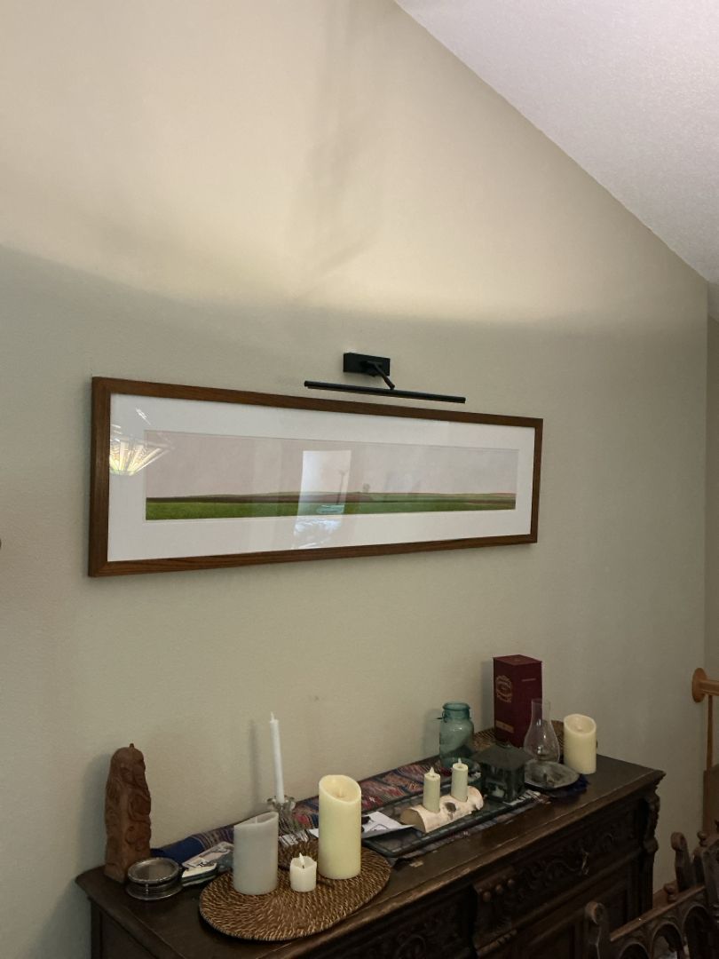 Long horizontal framed art on a wall with a light above it, over a wooden buffet table with candles.