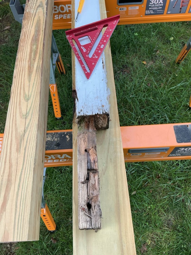 Decomposed wooden post being repaired with a speed square. The setting is outdoors on saw horses.