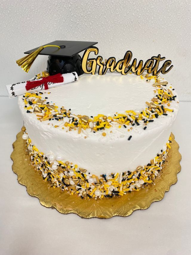 White graduation cake with gold sprinkles, gold base, and a cap plus Graduate topper