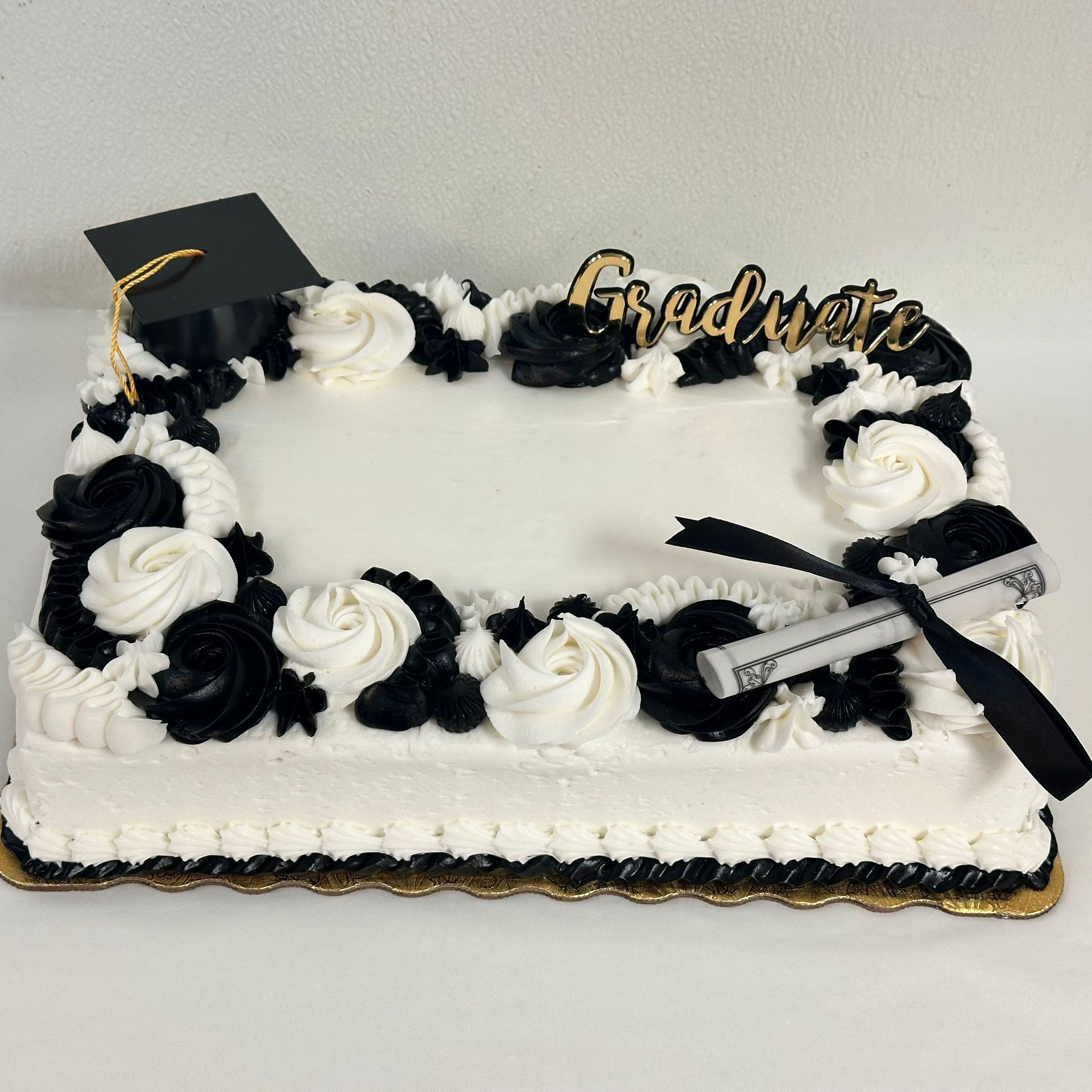 Graduation cake with black and white frosting, cap and diploma decorations, and “Graduate” topper