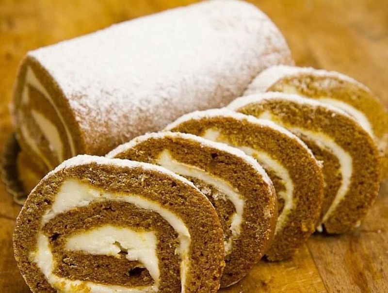 Sliced Swiss roll cake dusted with powdered sugar on a wooden board
