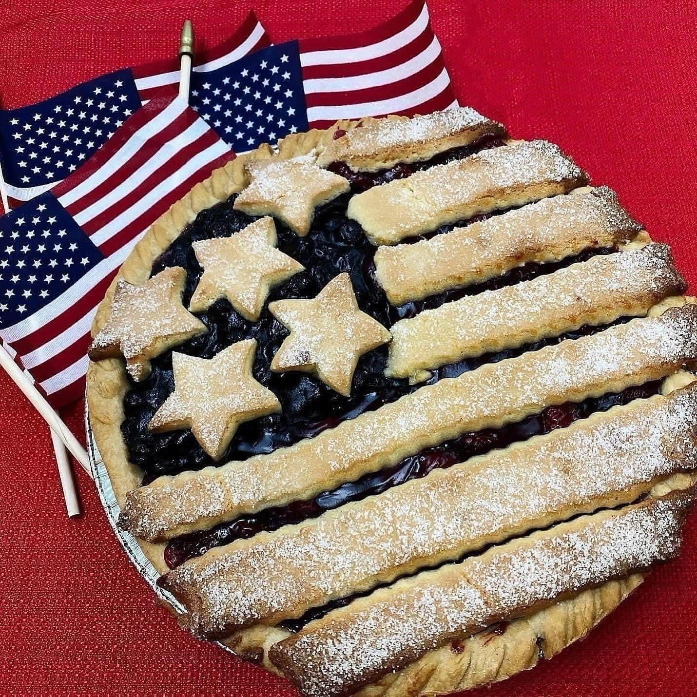 Patriotic star-shaped cookie with striped icing and powdered sugar beside small US flags on a red background