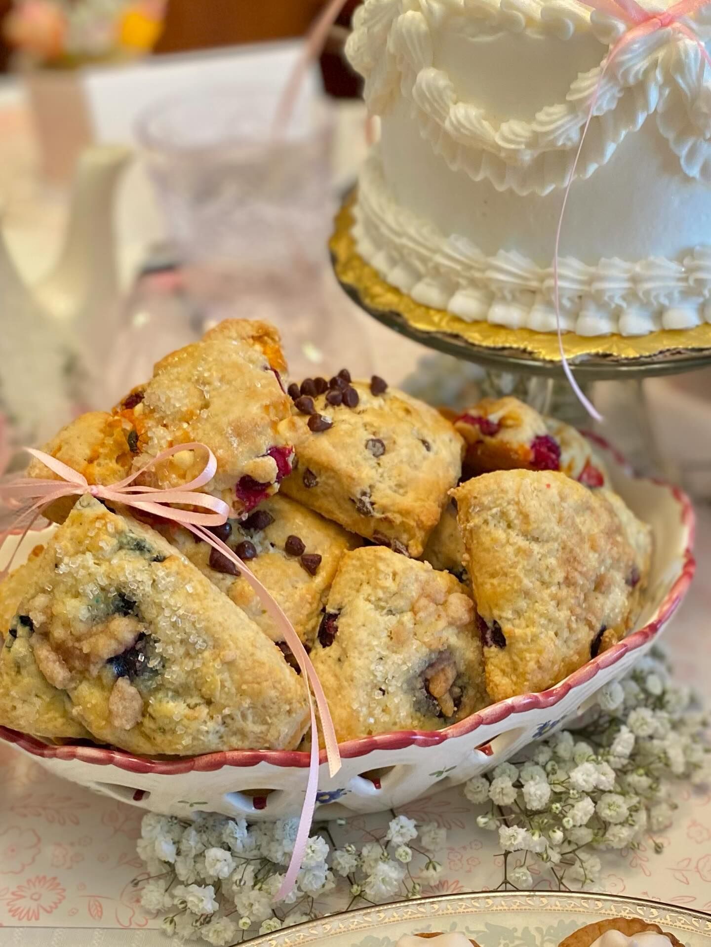 Basket of scones with chocolate chips and berries, tied with pink ribbon; cake in background.