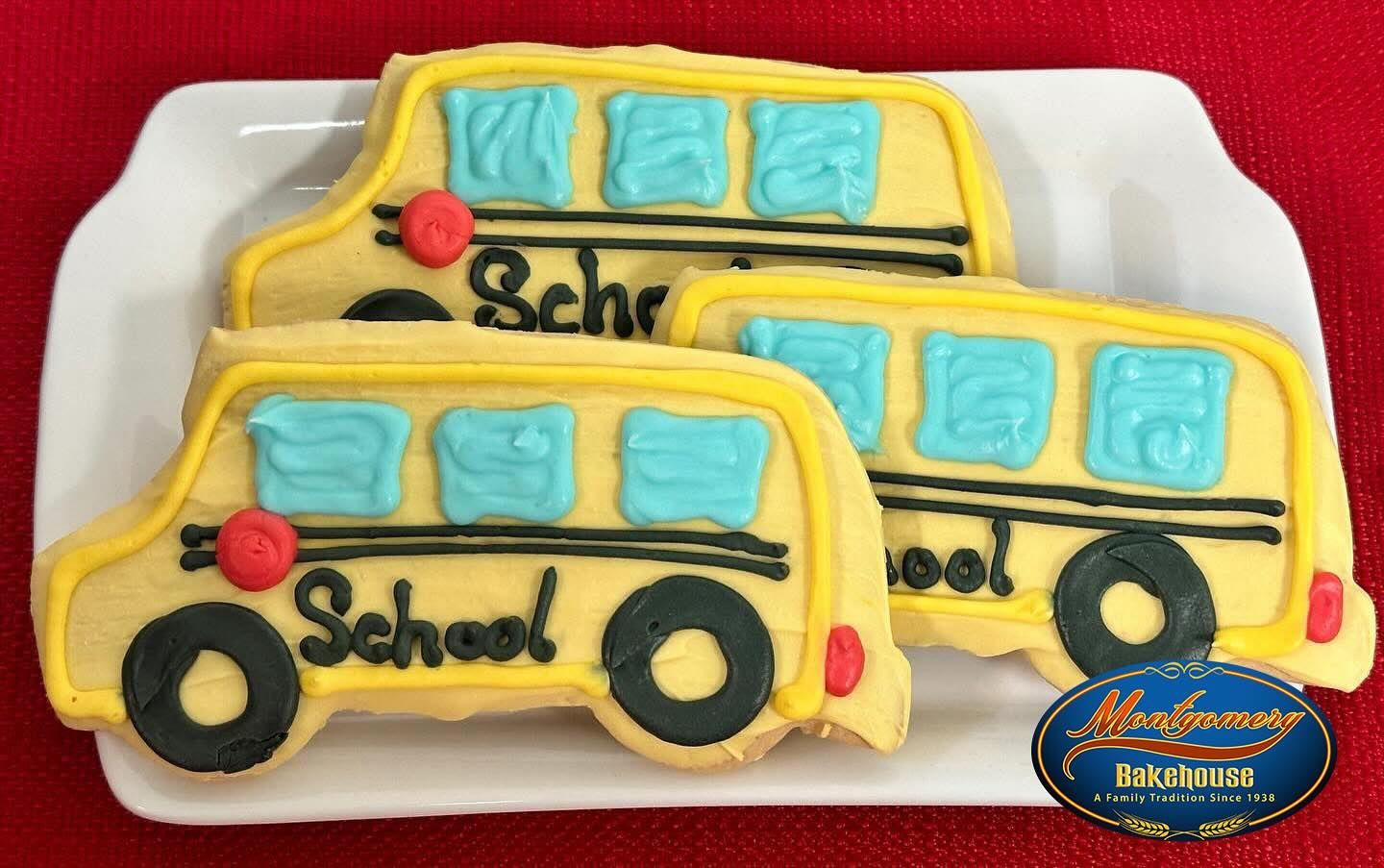 School bus-shaped sugar cookies, yellow with blue windows, on a white plate.