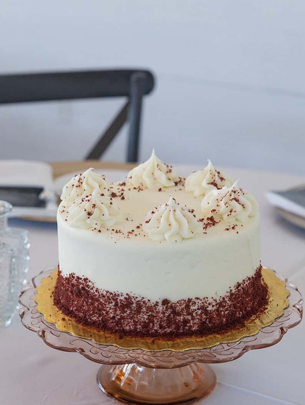 Red velvet cake with white frosting, on a glass cake stand.