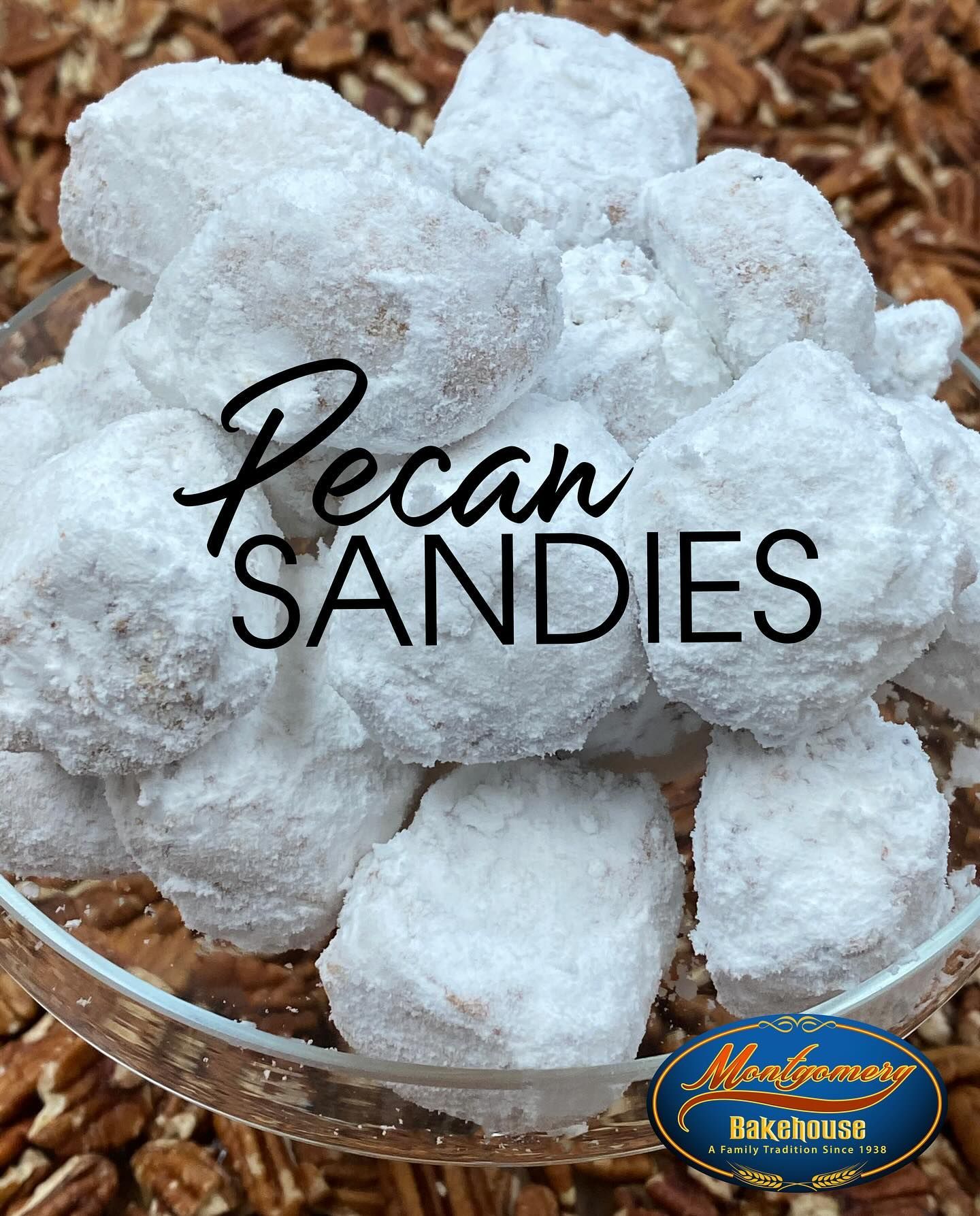Pecan Sandies cookies coated in powdered sugar, piled in a glass bowl on a bed of pecans.