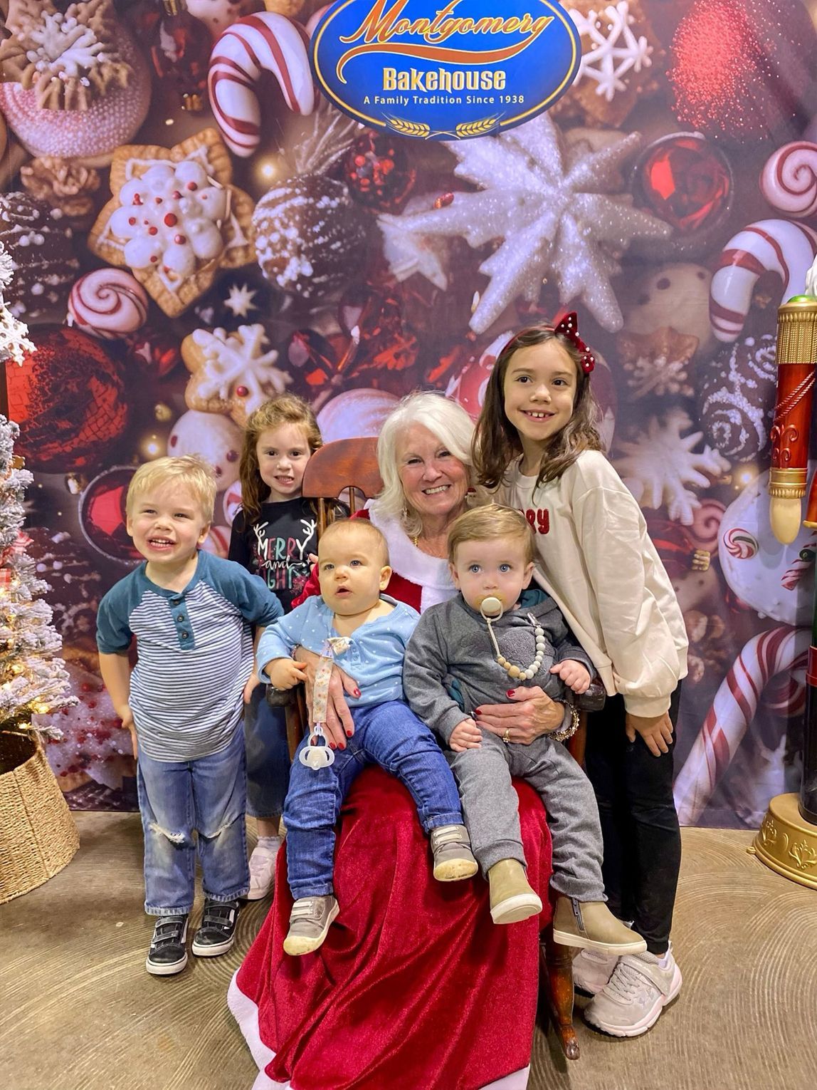 Santa Claus with six children in front of a holiday backdrop. Some children are seated in his lap.