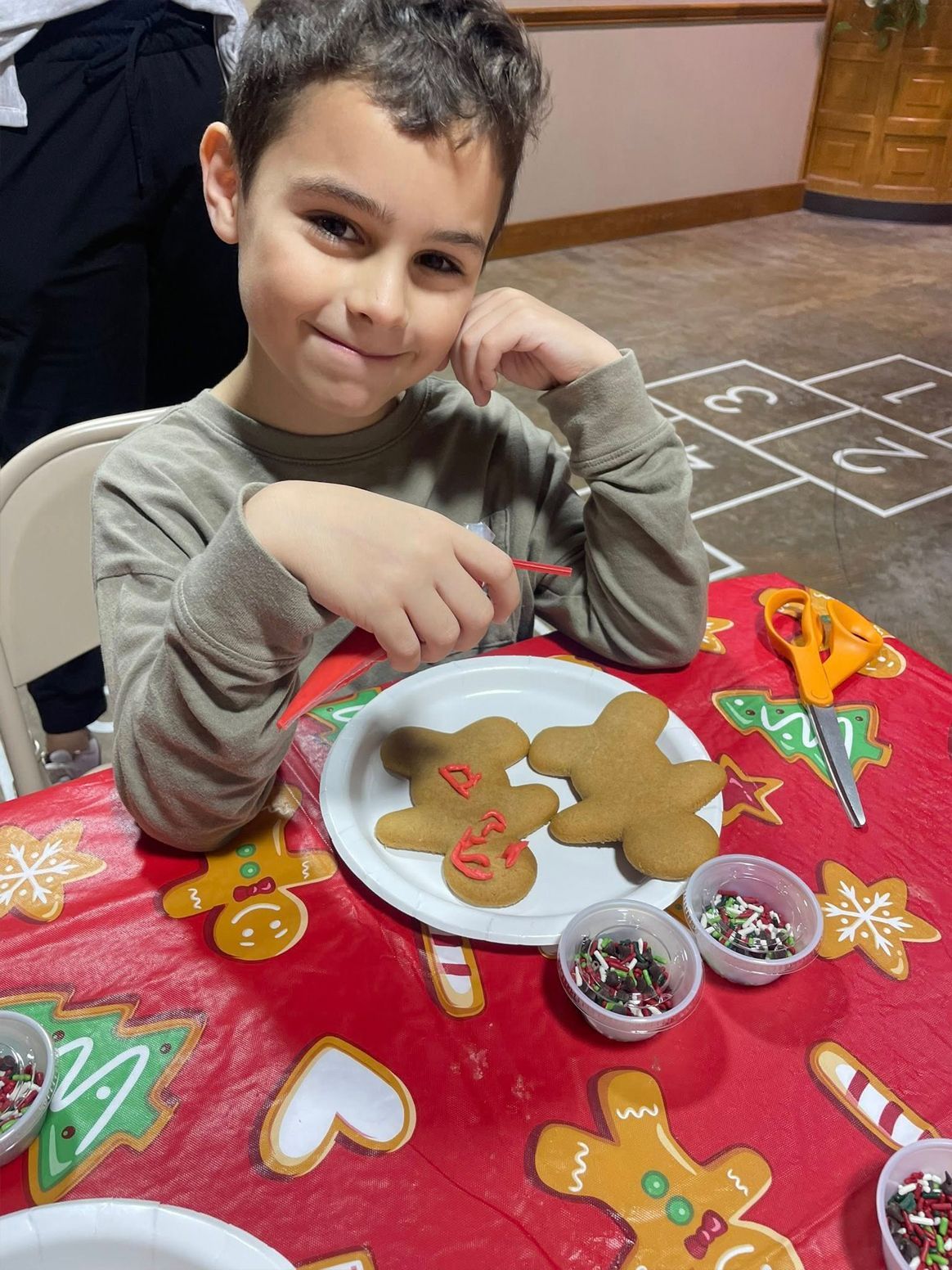 Boy decorates gingerbread cookies at a table covered with Christmas decorations.