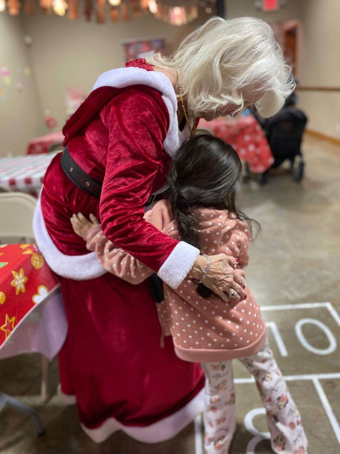 Woman in Santa suit hugging a child in a room with a party setting.