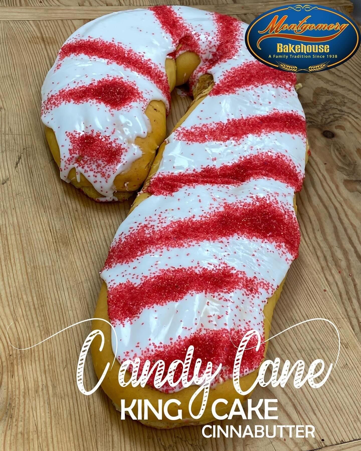 Candy cane-shaped King Cake, white icing with red sprinkles, on wooden surface.