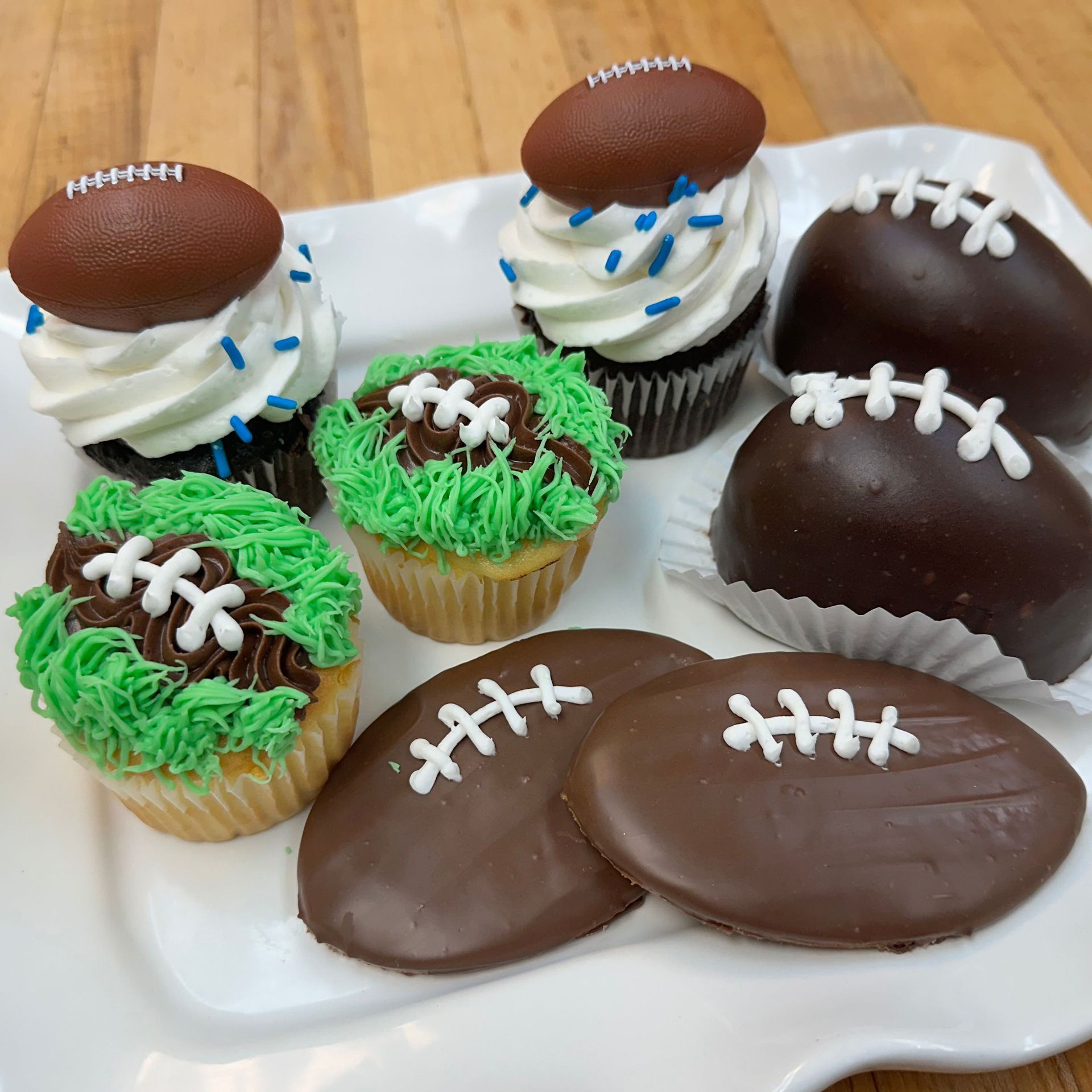 Football-themed cupcakes, cake pops, and cookies on a white plate. Chocolate frosting and green frosting resemble footballs and grass.