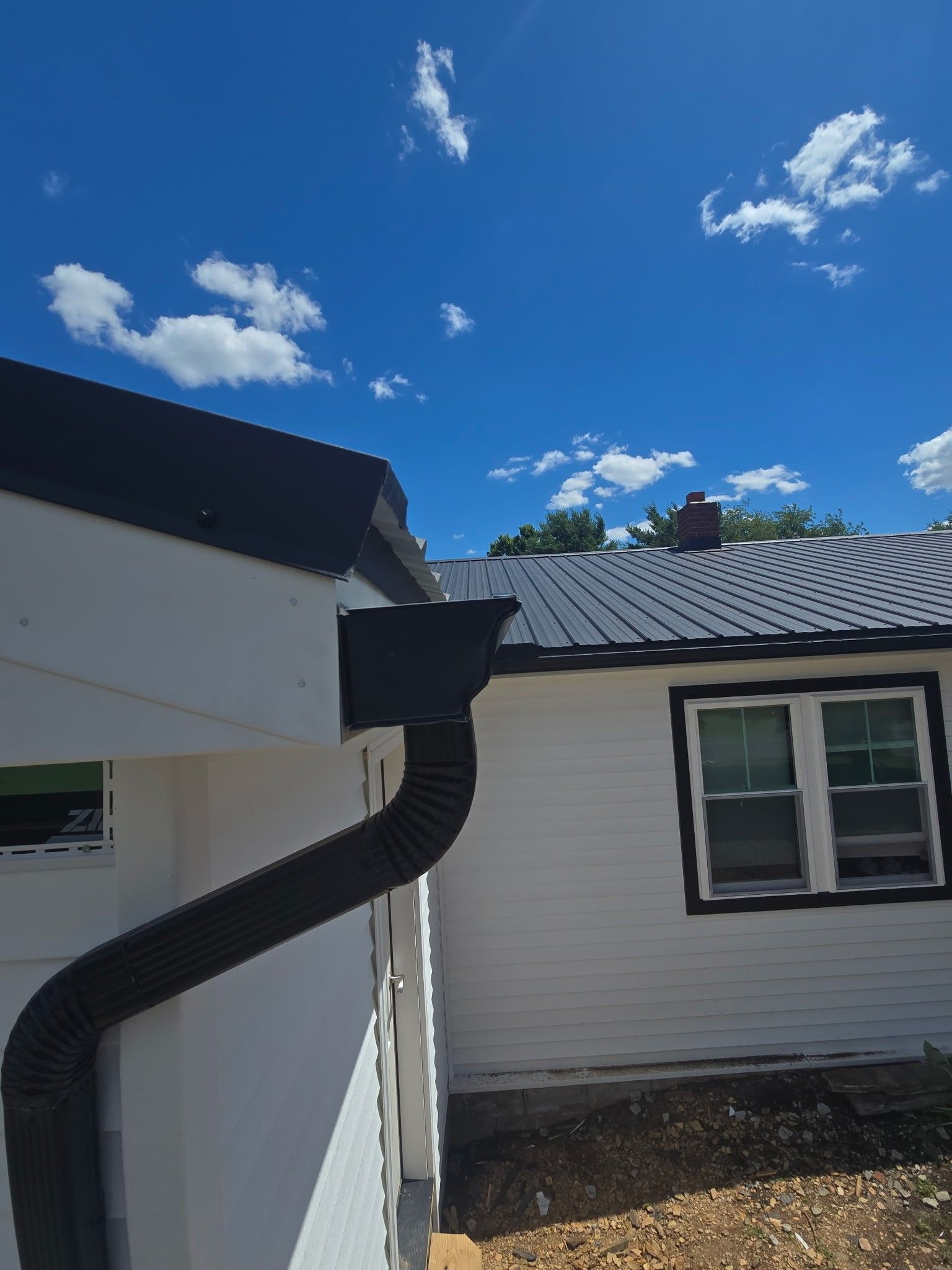 House roof and gutter under a bright blue sky with clouds