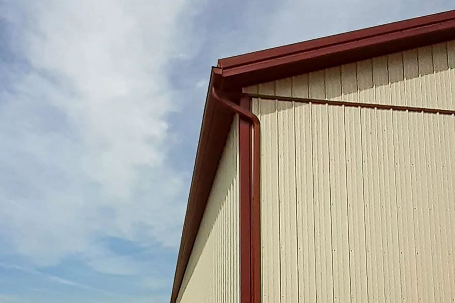 Beige barn siding with red trim against a cloudy sky
