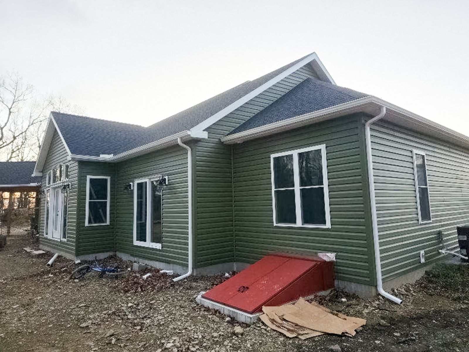 Green house with white trim and red ramp on a muddy construction lot