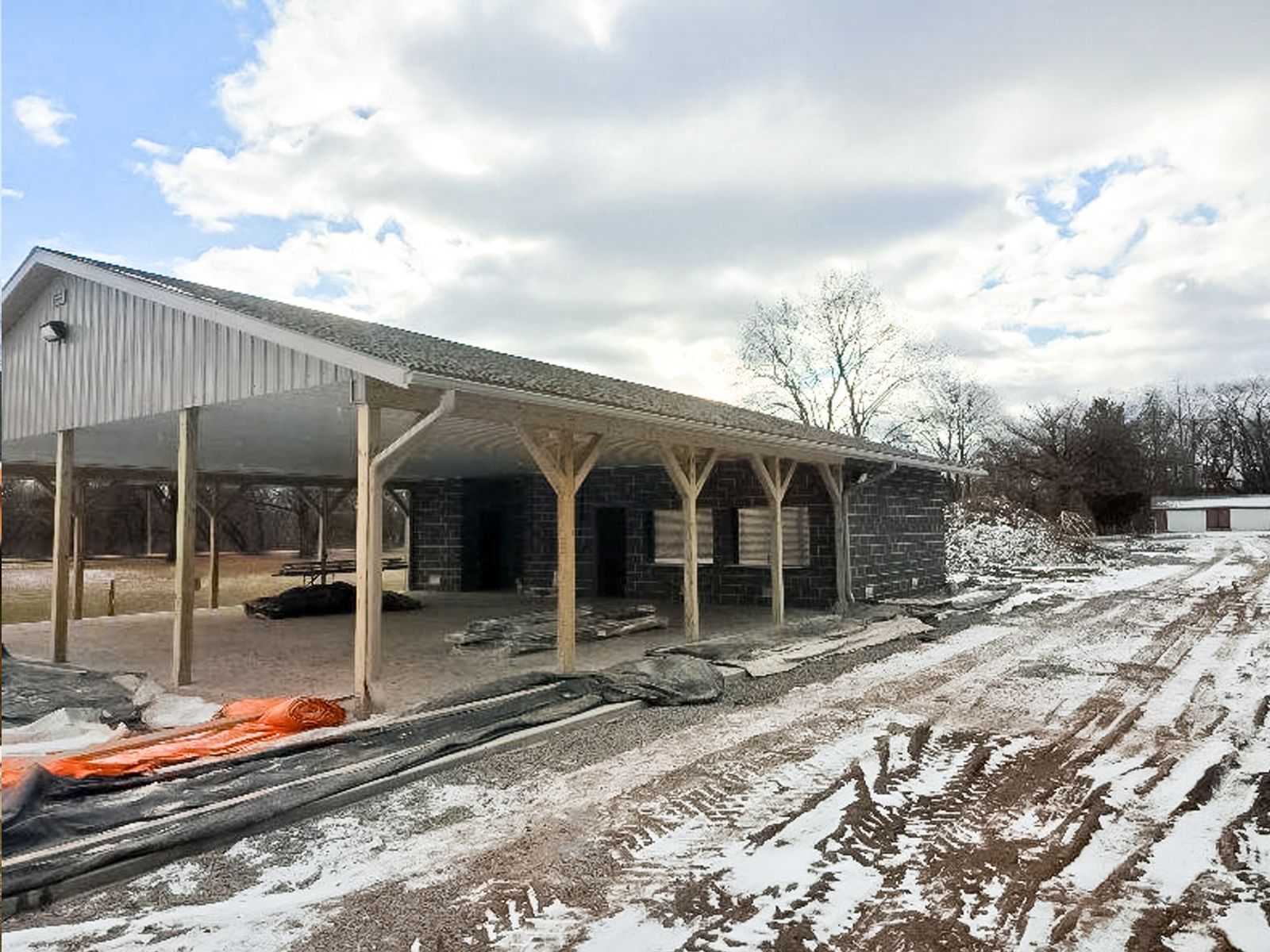 Open-sided barn with metal roof on a snowy, muddy farmyard under cloudy skies